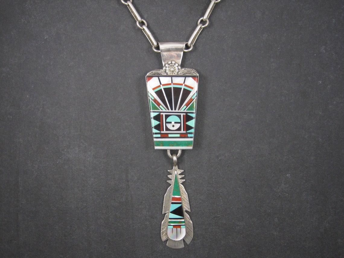 This huge vintage pendant is sterling silver.
It is the creation of Zuni silversmiths Lucy and Ricky Vacit.
It features mother of pearl, jet, coral and 2 different types of turquoise inlay.

The pendant measures a whopping 1 7/16 by 5 3/4