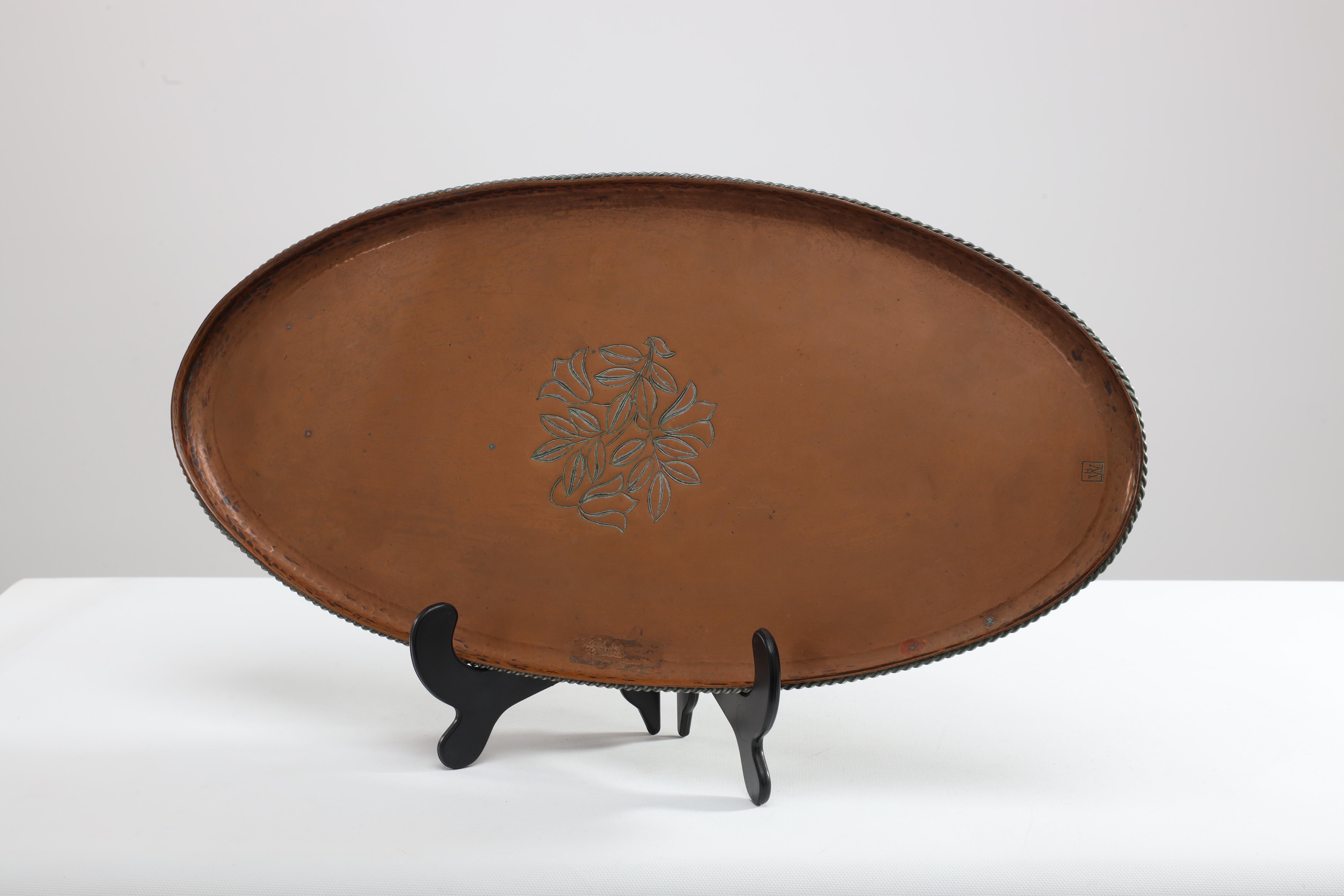 Hugh Wallis. An Arts & Crafts oval copper tray with rope twist edge and chased floral decoration to the centre. Stamped HW in a square. Hugh Wallis was based in Altrincham, near Manchester in the North-West of England, a highly skilled artist and