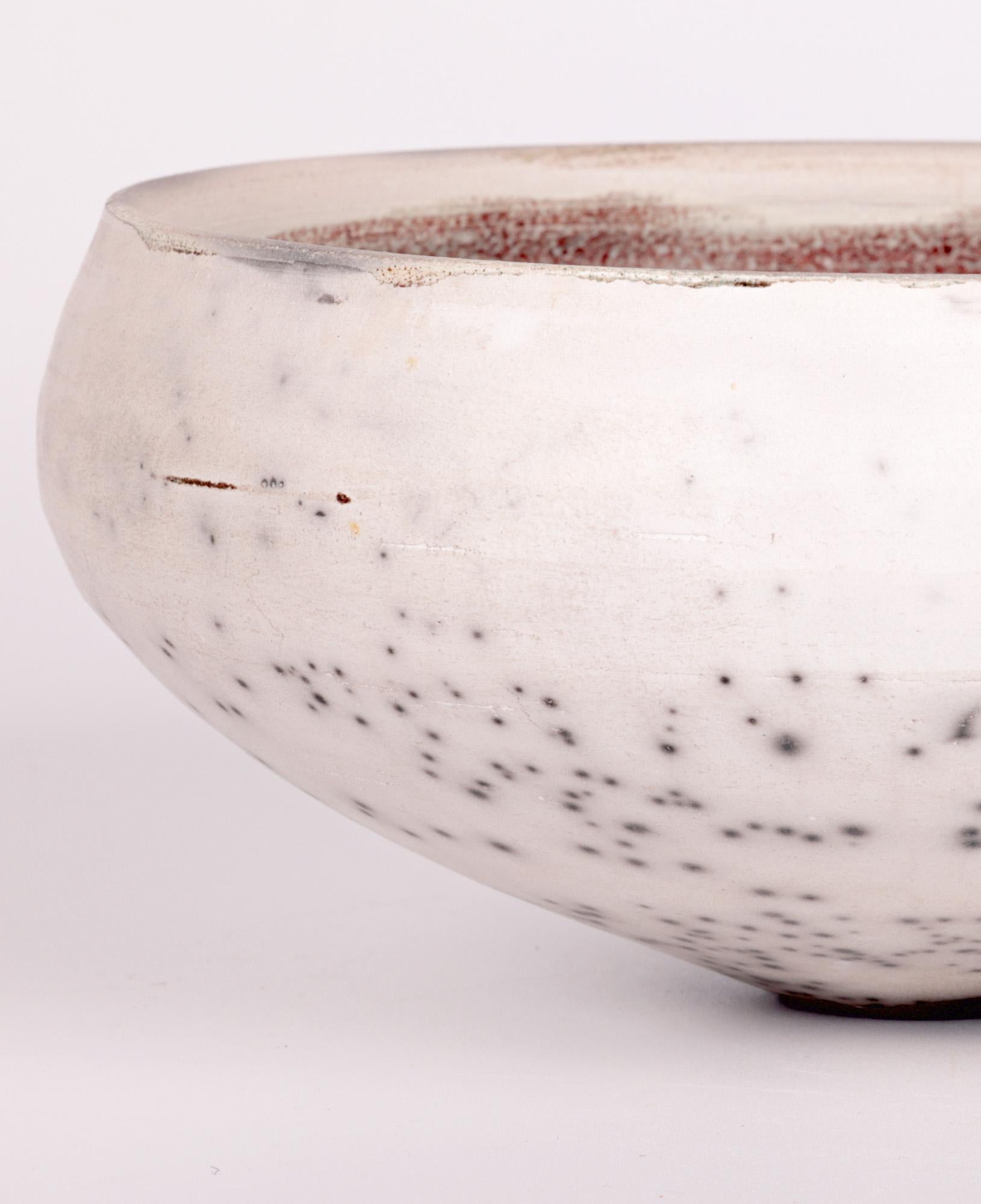 A stylish and large Carnon Downs Pottery raku bowl made during the 25th anniversary by renowned potter Hugh West (British, b.1950) and dating from 1996. The lightly hand potted bowl stands on a very narrow round foot and is of wide rounded shape