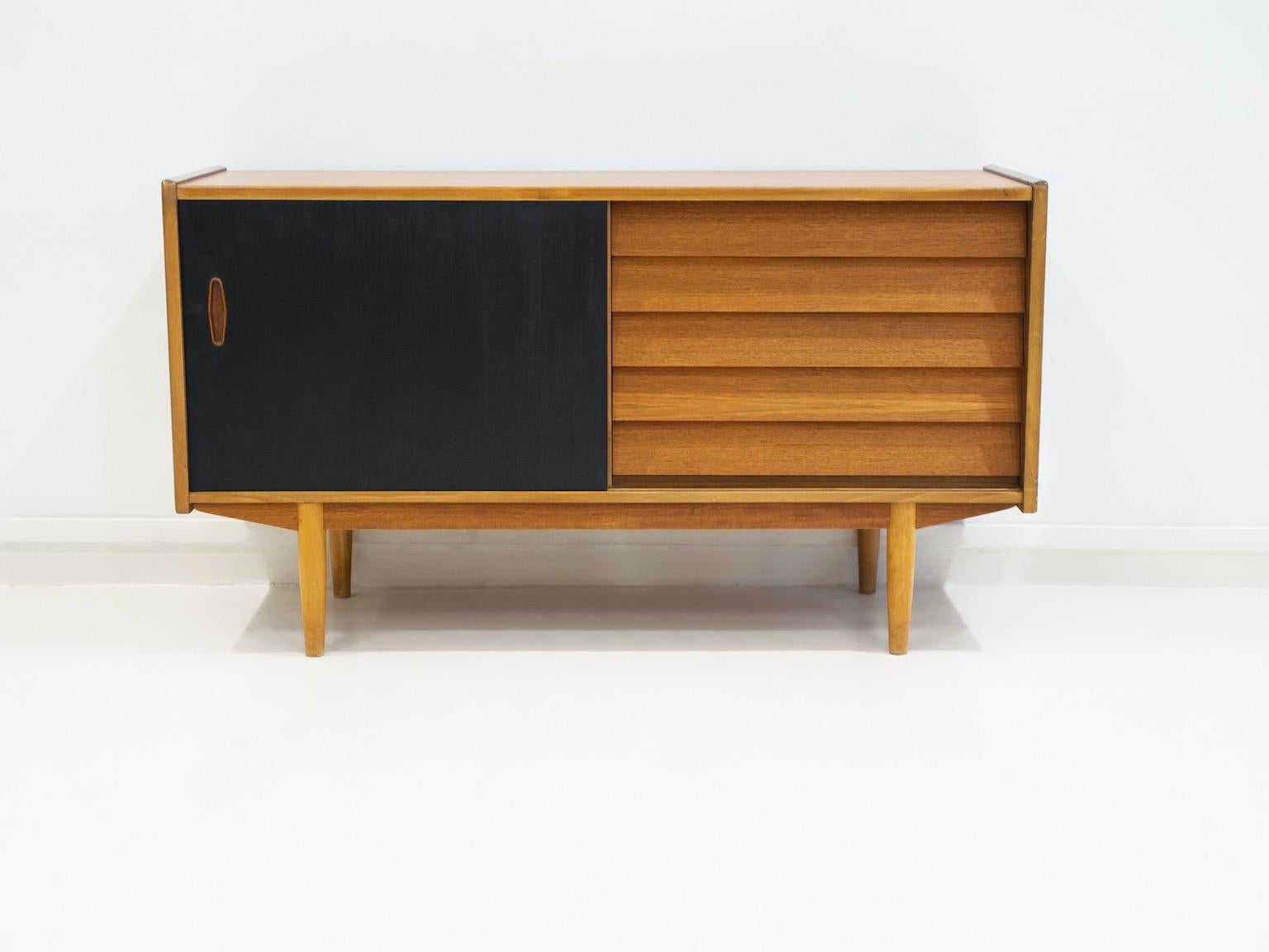 Teak sideboard with five drawers and a sliding door behind which is a storage compartment with a shelf. Manufactured by Hugo Troeds. Sliding door painted black at a later date.