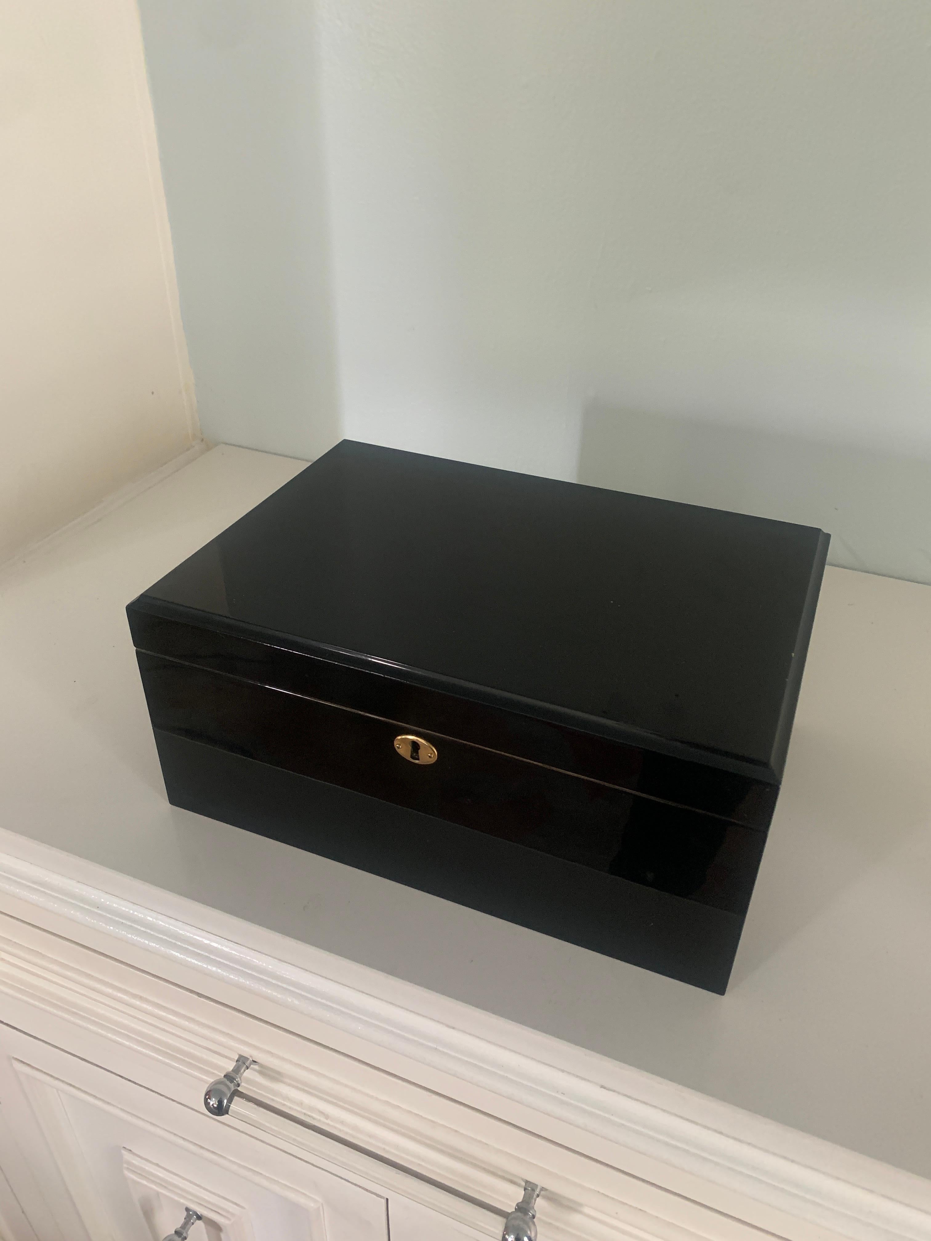 Large and highly polished black humidor with brass key detail. The Cedar lined interior reveals a shelf and will hold many cigars of varying size. Each level has removable sections to separate your Cuban from your fine home rolled!

The hinged top