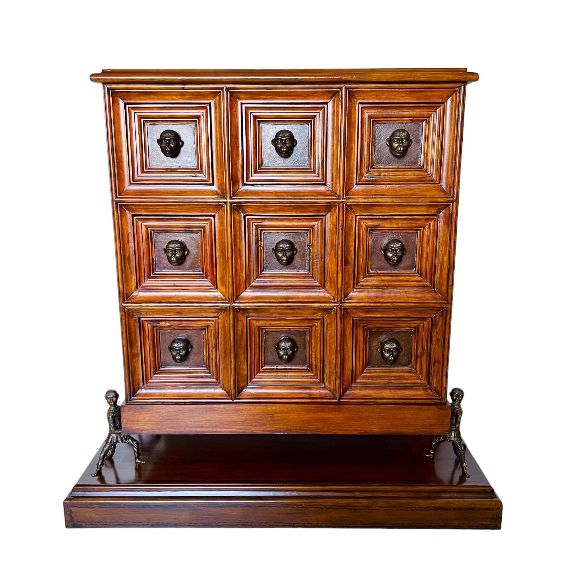 This late 20th century leather paneled brass mounted apothecary Humorous Chest in the manner of Theodore Alexander is styled after an original 19th century Italian design. It features nine framed drawers with resin monkey head pulls and a patinated