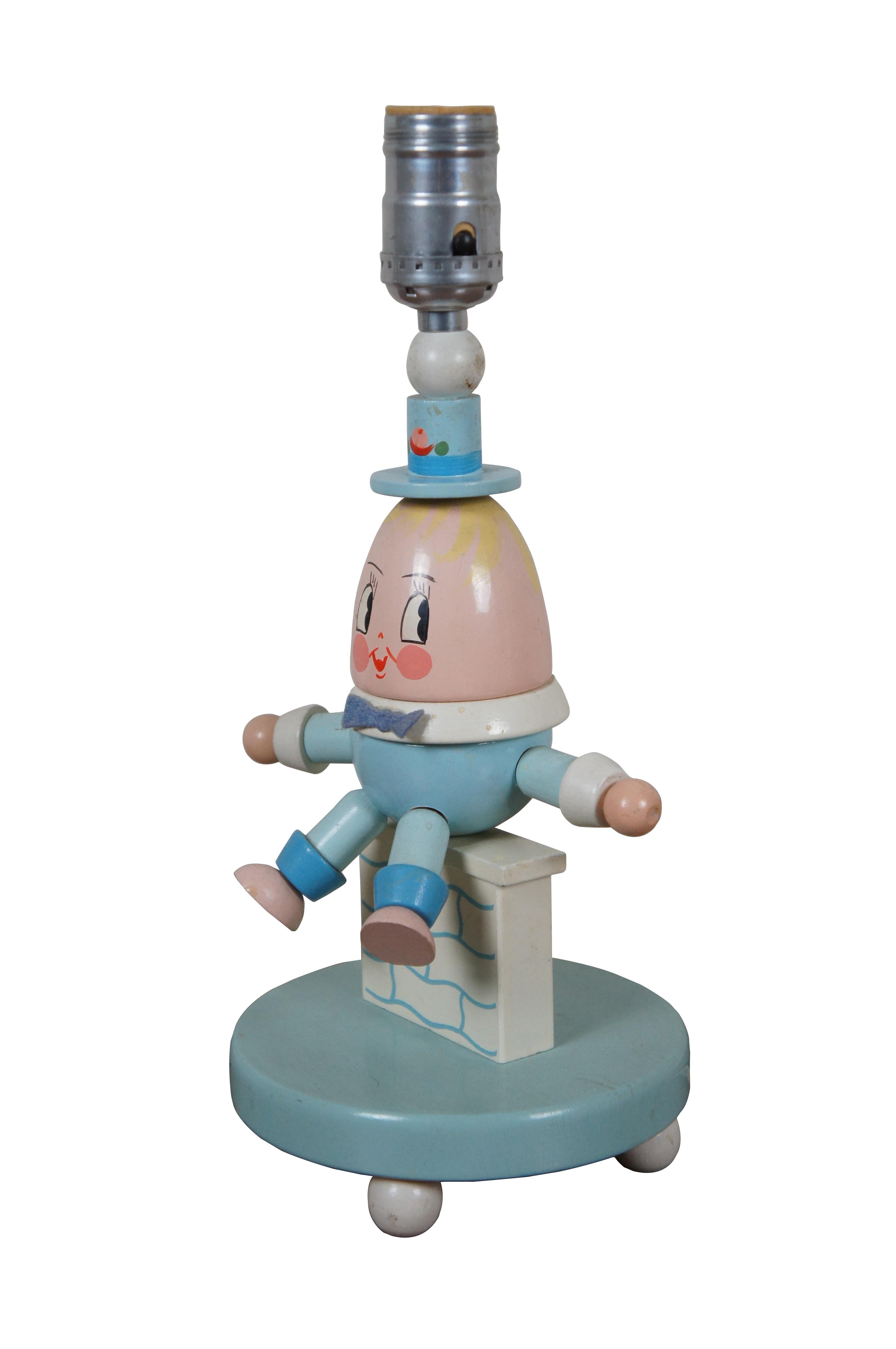 Circa 1960's painted wooden figural table lamp featuring the egg shaped nursery rhyme character Humpty Dumpty, dressed in a powder blue suit and top hat, seated on a white and blue wall. Manufactured by Nursery Plastics Inc.

Dimensions:
6.25