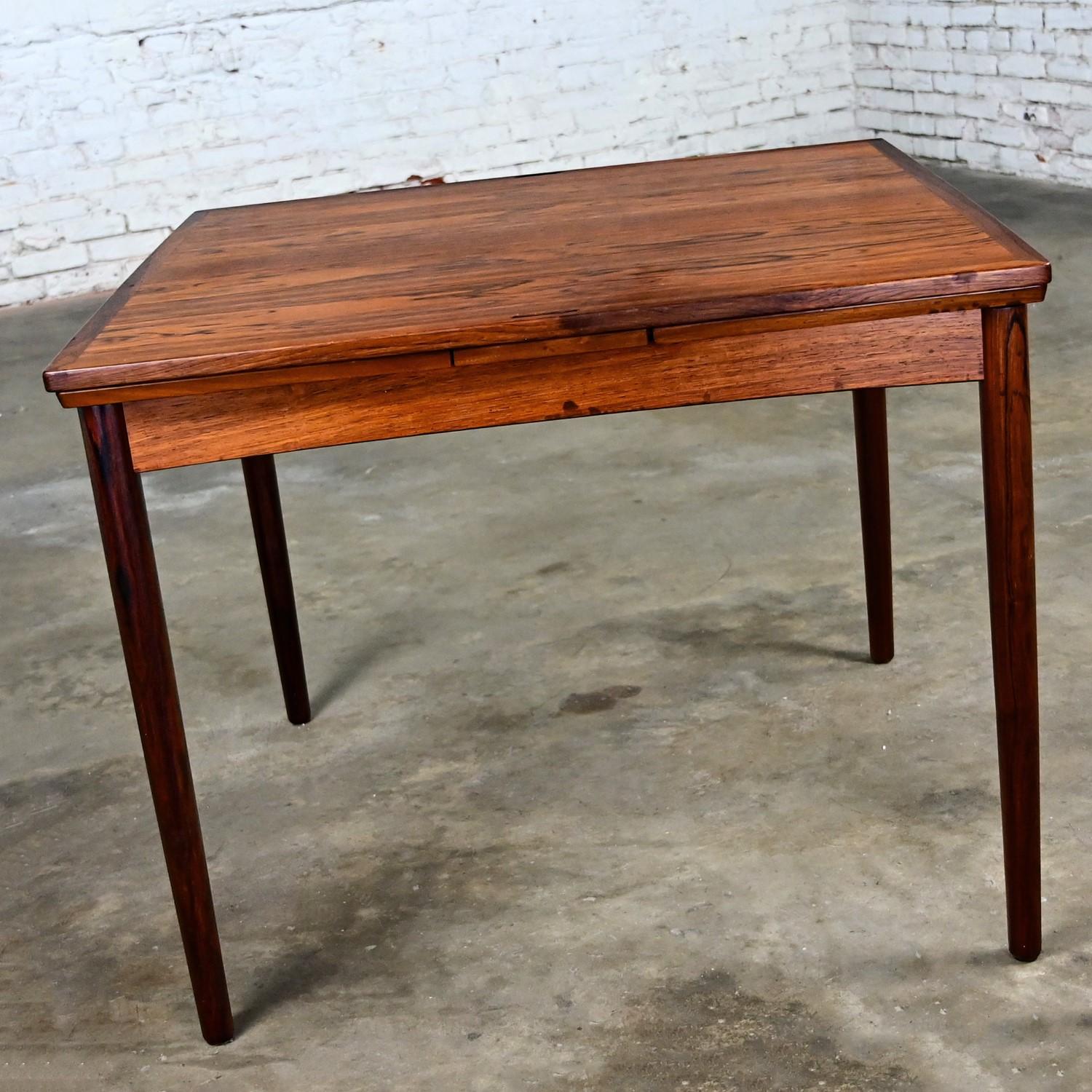 Handsome vintage Scandinavian Modern expanding flip top Rosewood dining table designed by Carlo Jensen for Hundevad & Company. Comprised of solid rosewood & rosewood veneer, black faux leather, and two table leaves. Beautiful condition, keeping in