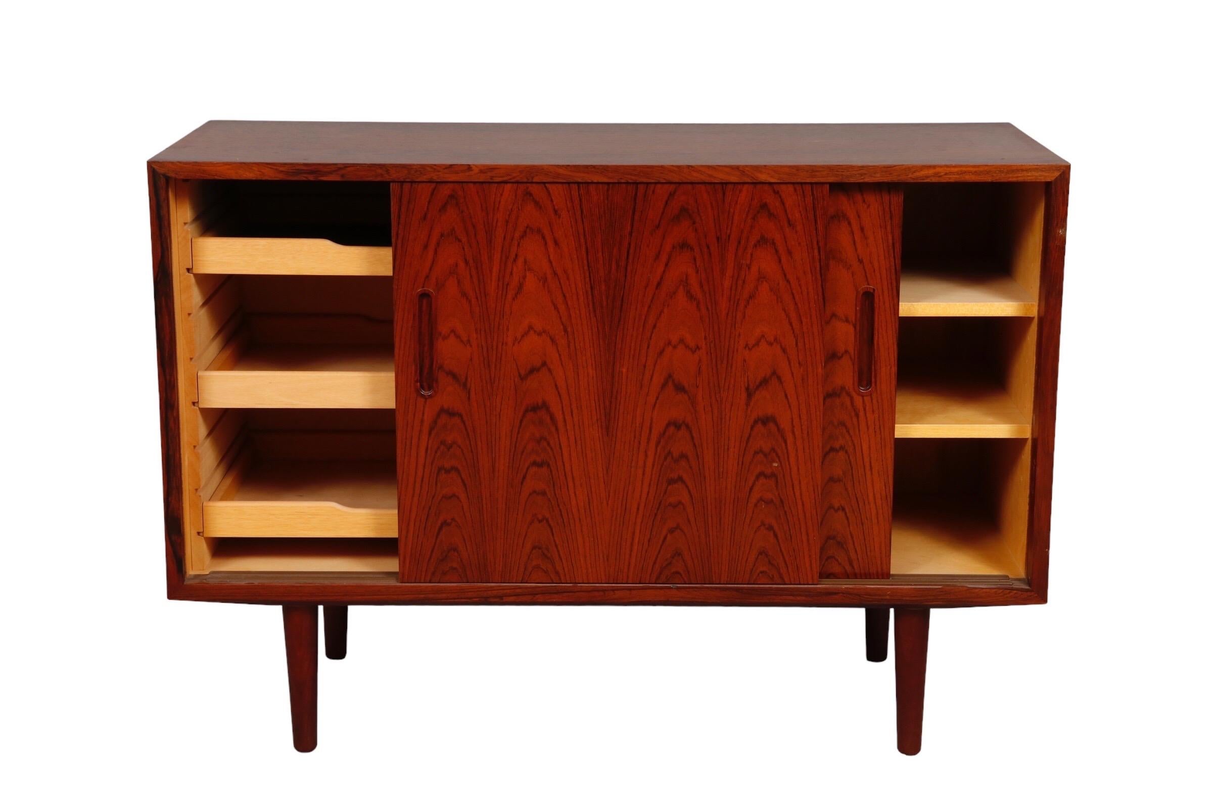 A Mid-Century Modern sideboard by Poul Hundevad. Made of beautifully grained rosewood. Bookmatched sliding doors reveal two shelves to the right and three pull out shelves to the left. Finished with round tapered legs. Marked HU Made in Denmark in