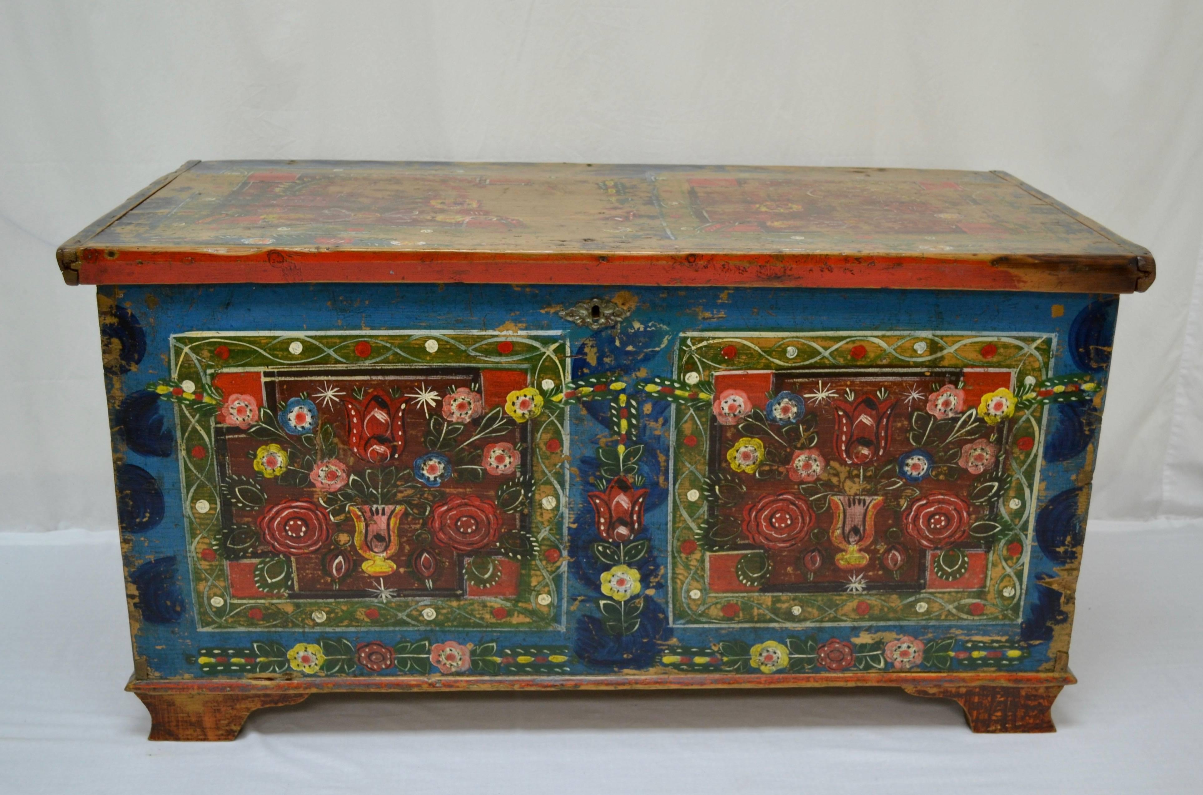 A piece of relatively plain box construction, with no embellishments to the woodwork, this hand-cut dovetailed pine trunk or blanket chest is distinguished by the riot of colour on its front and top. On a bright blue ground are two painted panels,