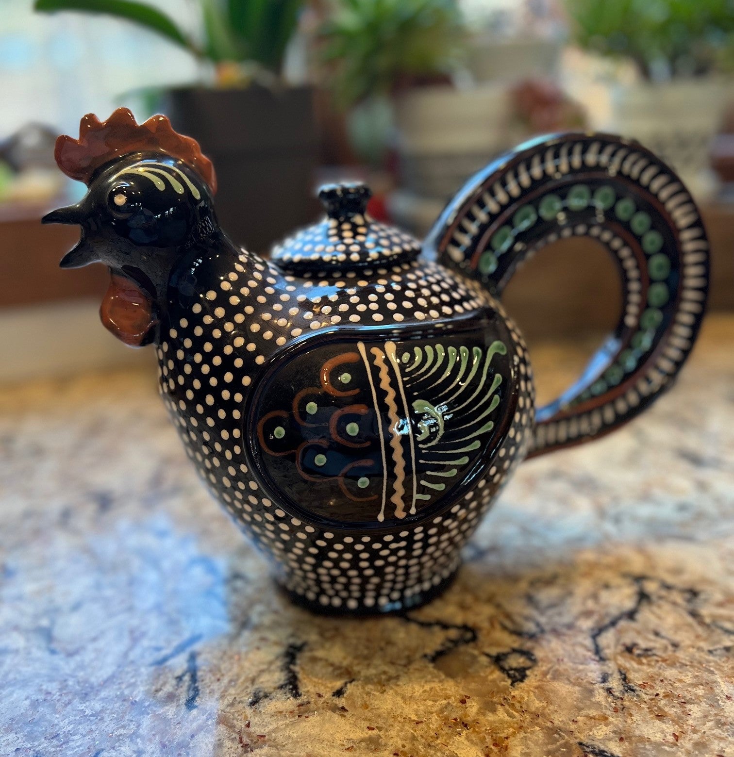 A Hungarian Folk Art Red Ware Rooster Lidded Jug/Teapot by Imre Szűcs. A black/brown based rooster decorated with white dots and green, yellow and red painted elements.  The spout is in the beak. The inside of the teapot is glazed red ware. The