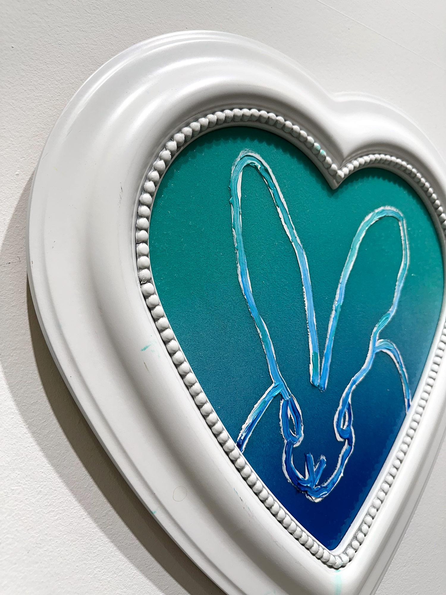 A wonderful composition of one of Slonem's most iconic subjects, Bunnies. This piece depicts a double bunny on a turquoise blue gradient background with thick use of paint and diamond dust. It is housed in a wonderful white heart shaped frame.