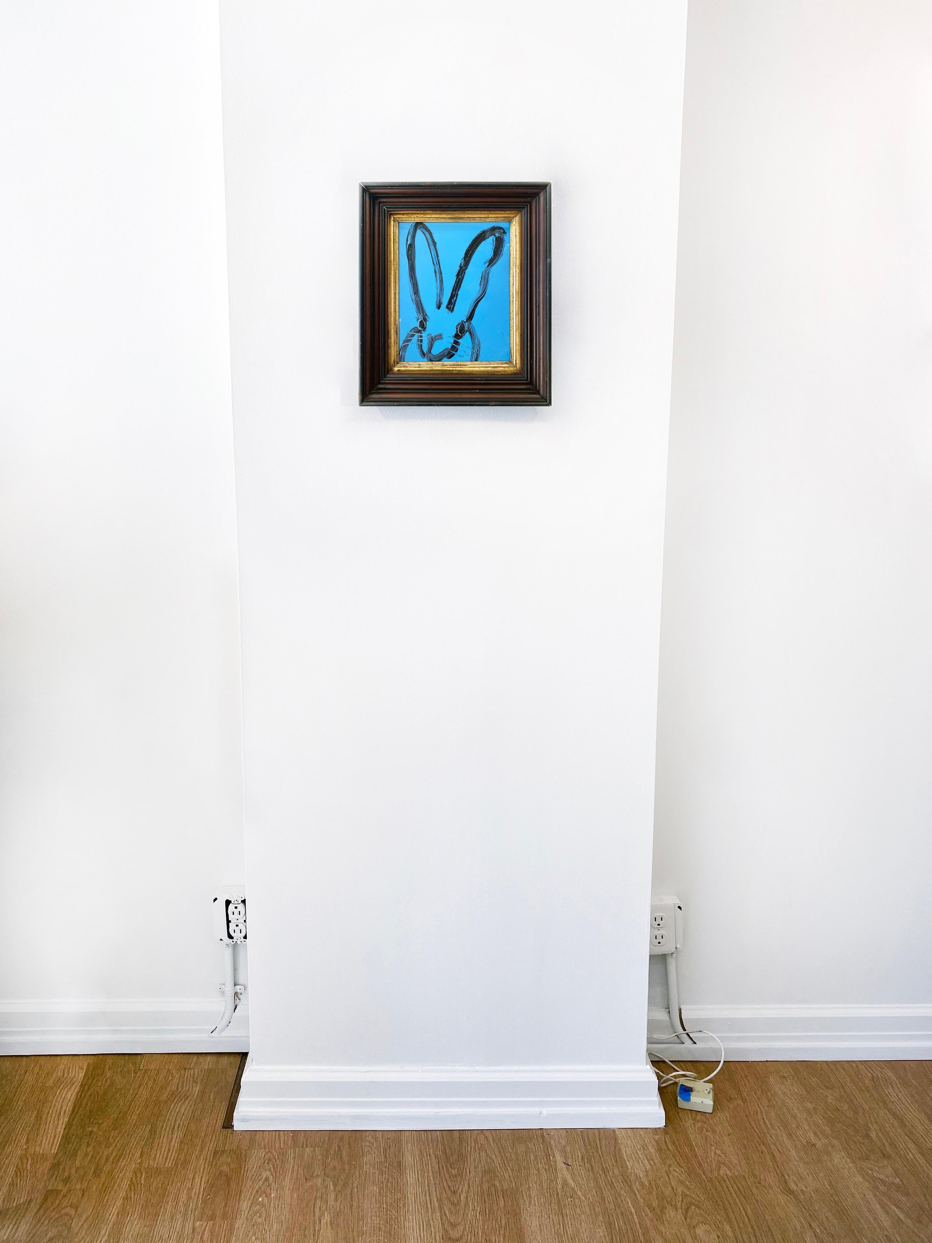 'Blue Tangle 2' by Hunt Slonem, 2021. Oil on wood, 10 x 8 in. Framed size is 14 x 12 in. This painting features Slonem's signature charming bunny outlined in black on a bright blue background. The expressive bunny features long slender ears and
