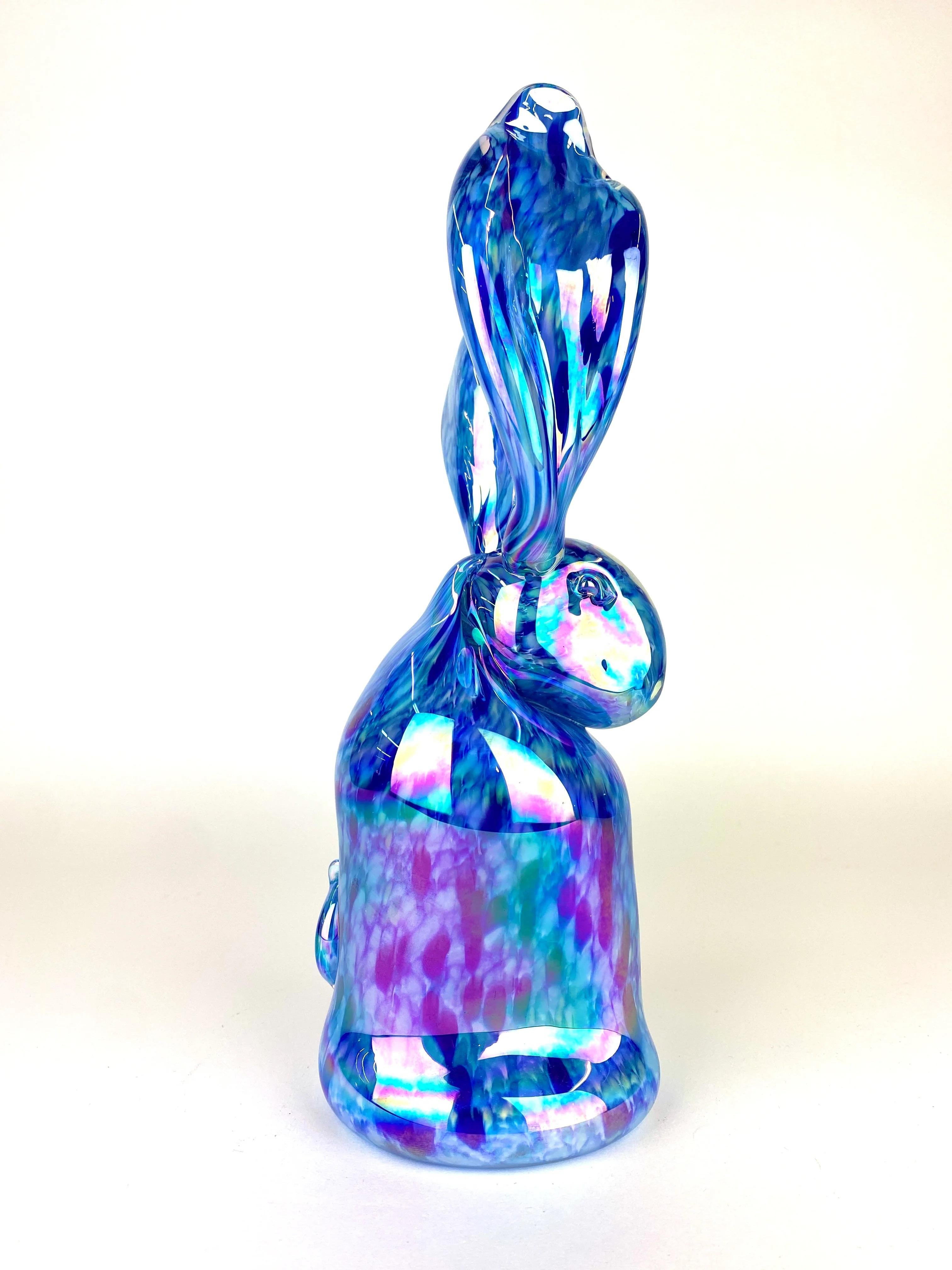 Hunt Slonem’s Caeruleus VI (2024) is a mesmerizing blown glass sculpture measuring 11.5 x 6 x 4 inches, showcasing a radiant, holographic bunny rendered in glossy, translucent glass. The sculpture shimmers with an enchanting interplay of