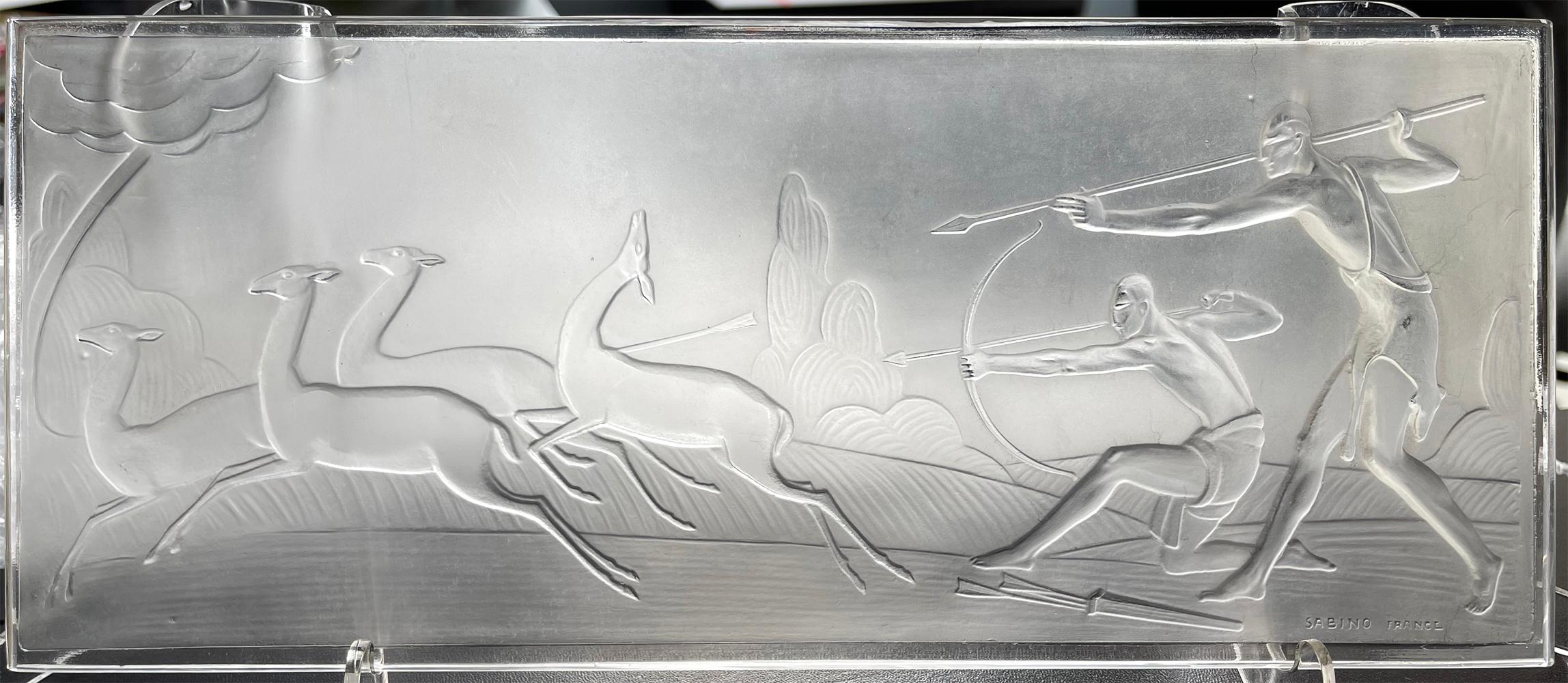 Beautifully sculpted and crisply molded by the famed Sabino glass company in Paris, using the milky or frosted glass that the company was known for, this panel depicts two semi-nude figures hunting a herd of deer or gazelles, with Art Deco trees and