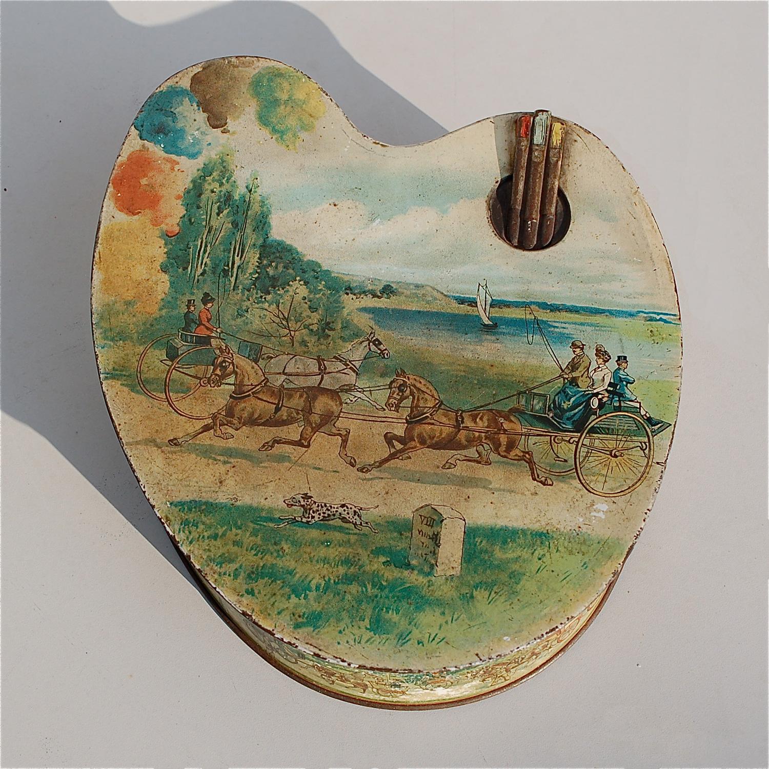This Huntley and Palmers antique biscuit tin dates back to circa 1900. It is shaped like an artist palette, featuring details like paint brushes peeping through the thumb hole, a small arrangement of paints ready for mixing, ... , The main