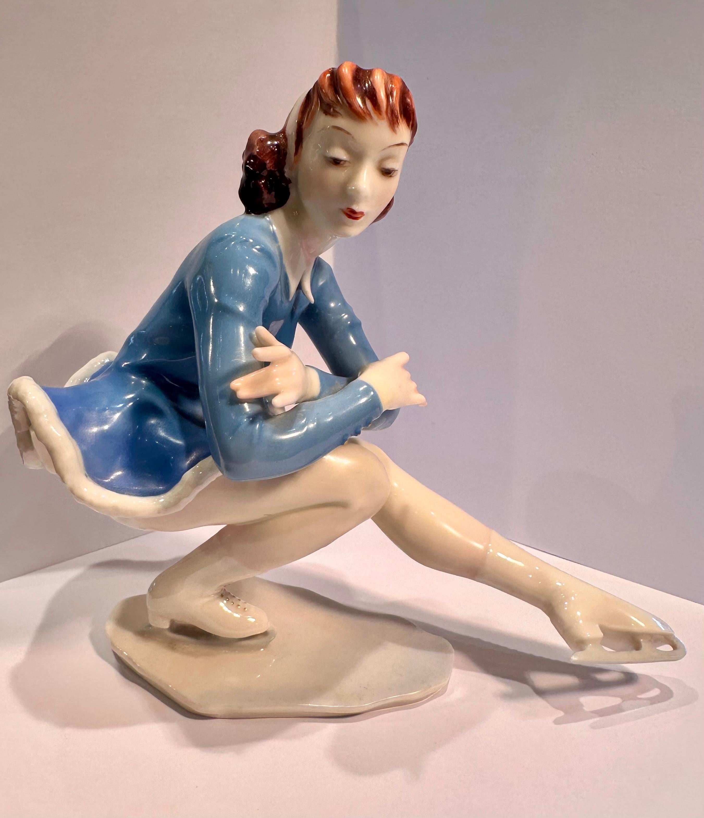 Collectible, hand made and hand painted in Germany Hutschenreuther fine quality porcelain Ice Skater figurine wearing a blue short ice skating dress with a depicted fur bottom, a white head band on head and ice skates.  She appears to be in a