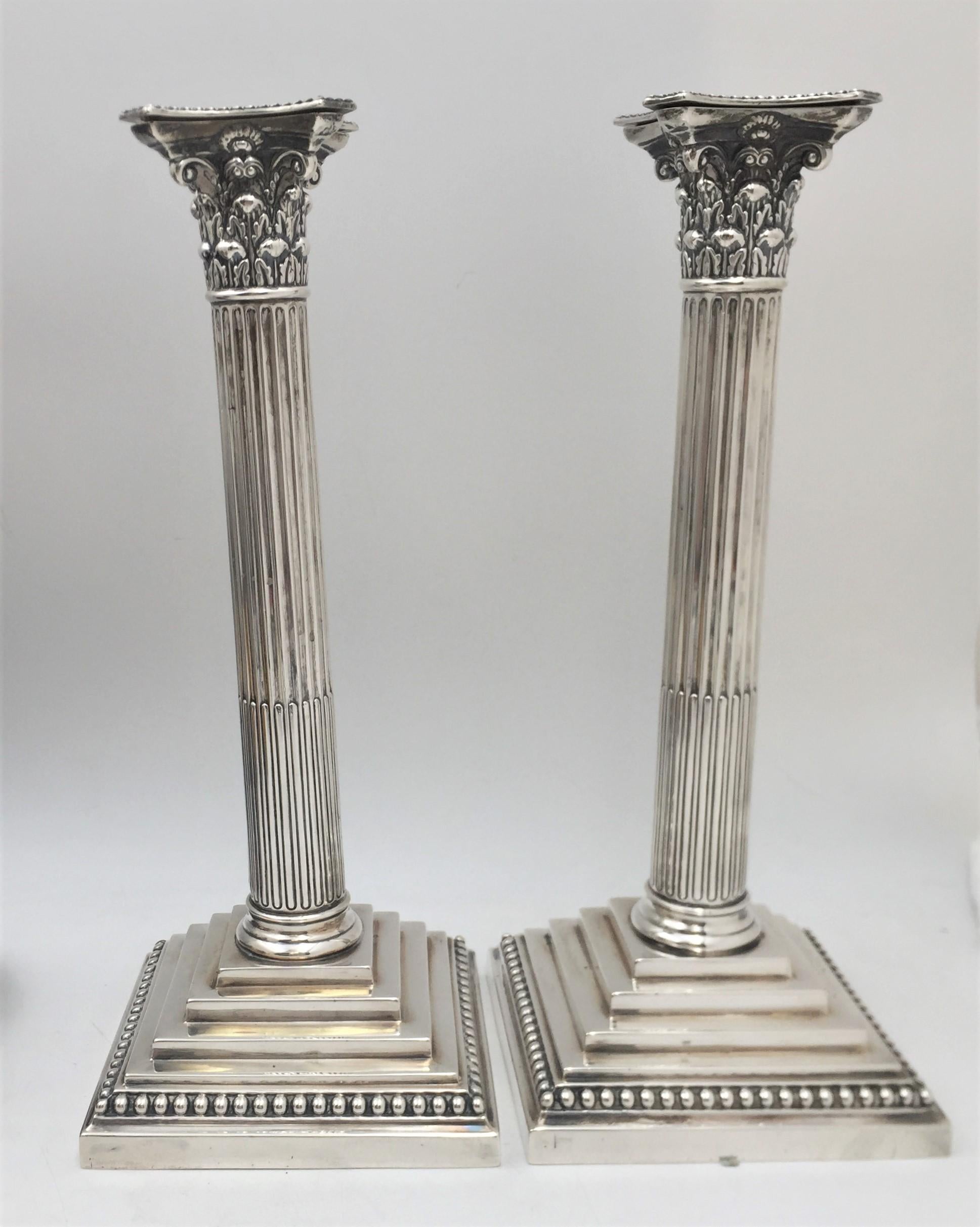Edward Hutton pair of sterling silver candlesticks from 1893 in Neoclassical style from the Victorian era. Elegantly designed as Corinthia columns standing on a square base with a beaded rim, these candlesticks measure 12'' in height by 4 1/2'' in
