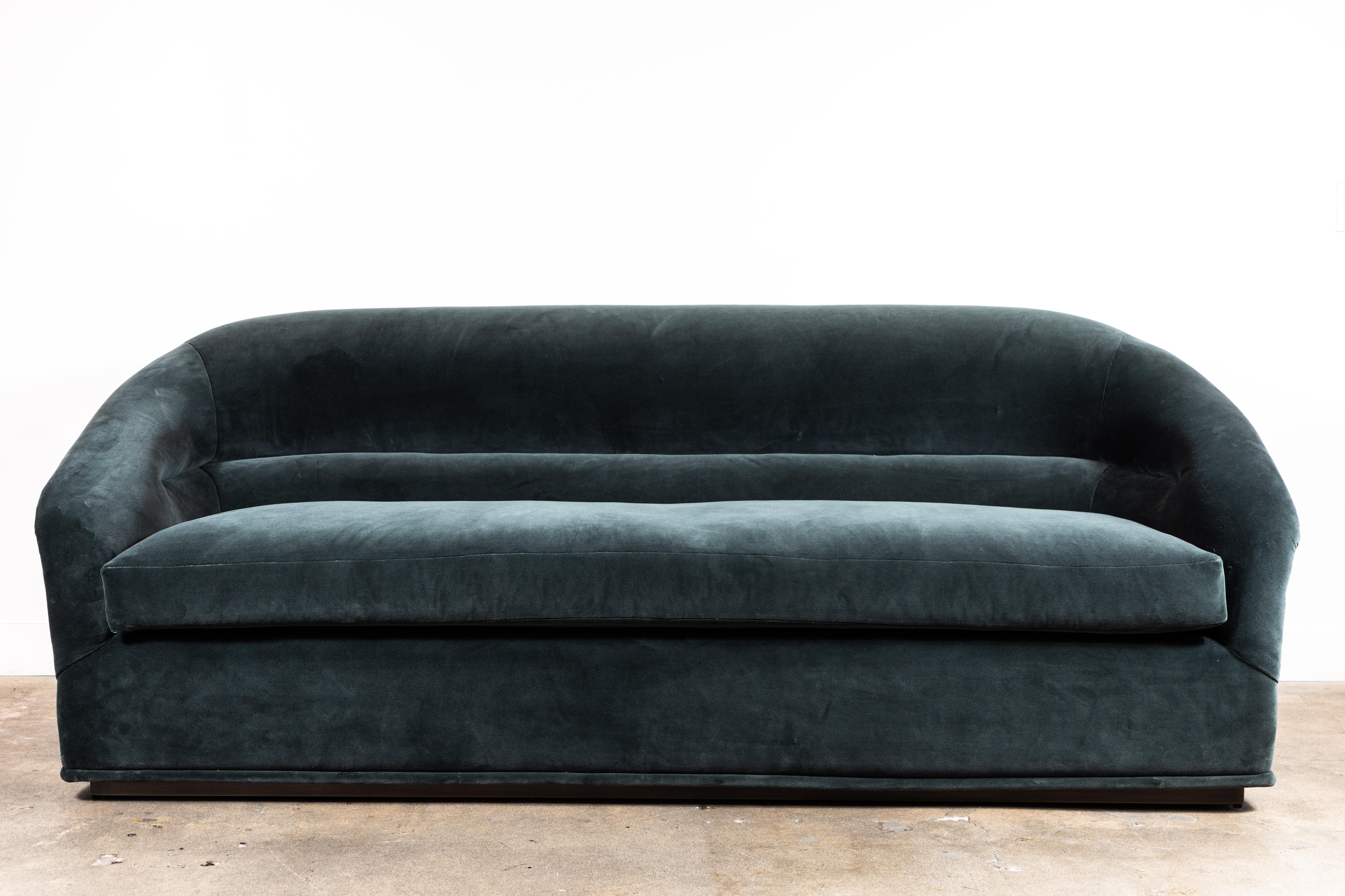 Velvet Huxley Sofa by Lawson-Fenning. The Huxley sofa is inspired by 1970s lounge furniture. A curvaceous form with a single line tuft and long seat cushion rest atop a polished brass base. 

The Lawson-Fenning Collection is designed and handmade in