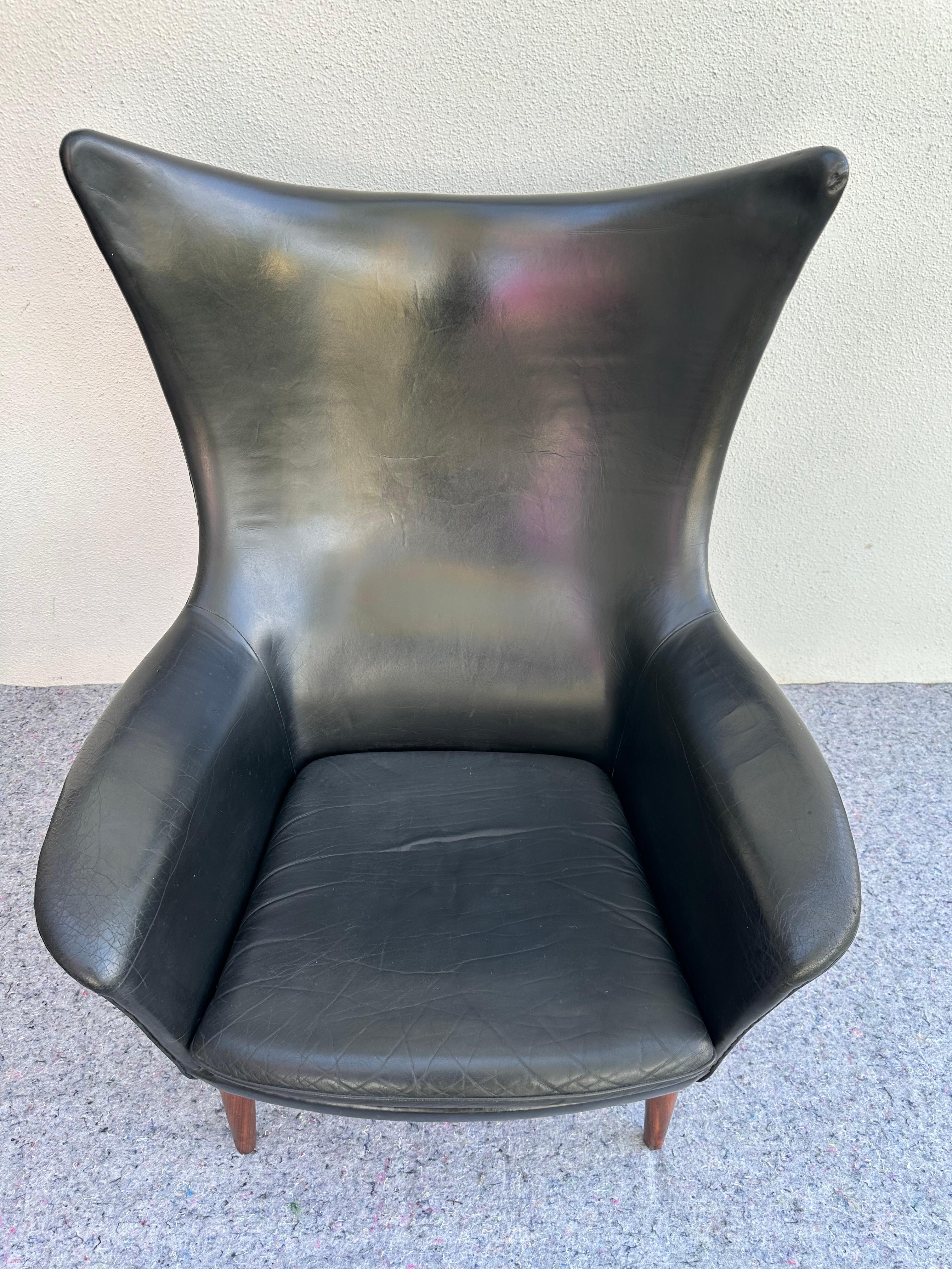 La HW Klein Bramin Lounge Chair & Ottoman in pelle nera danese è uno splendido pezzo di arredamento moderno di metà secolo. Una rivisitazione esagerata del design classico della sedia con schienale ad ala, in stile Mid Century Modern. Questo set