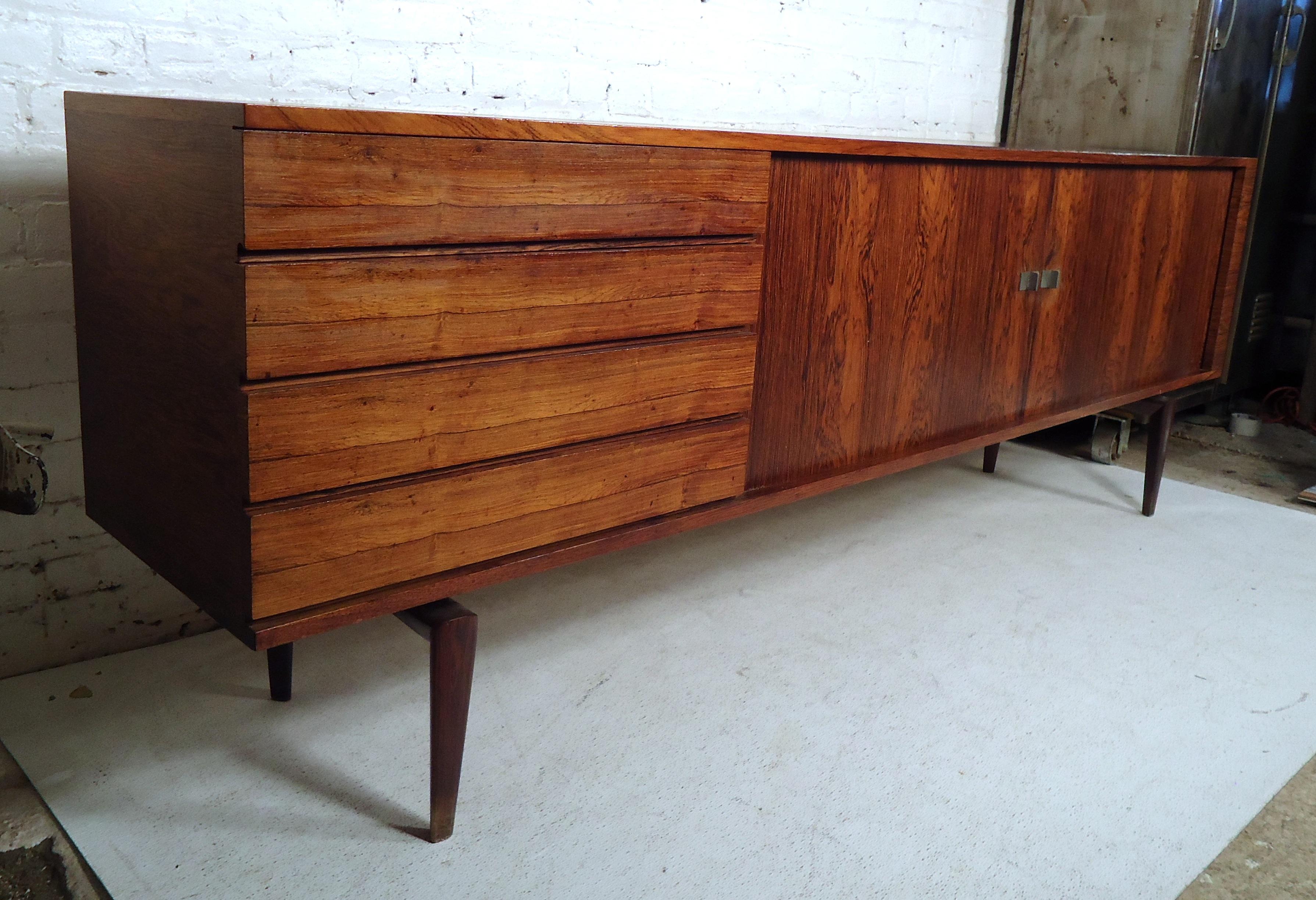 This stunning vintage modern sideboard offers plenty of room for storage within its four drawers and large storage compartments with shelves hidden behind its sliding doors. An elegant rosewood wood grain throughout and sturdy legs showing quality