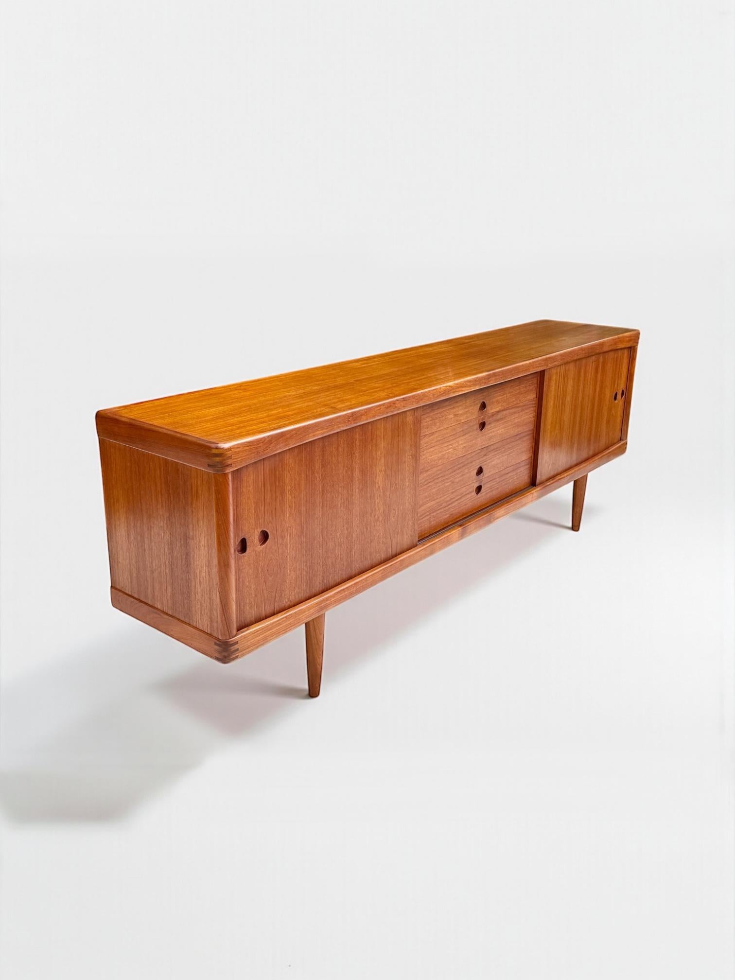 This iconic teak sideboard designed by HW Klein for Bramin, featuring a long, streamlined profile with finely crafted joinery at the corners. The sliding doors reveal generous storage space, complemented by central drawers with recessed handles.
