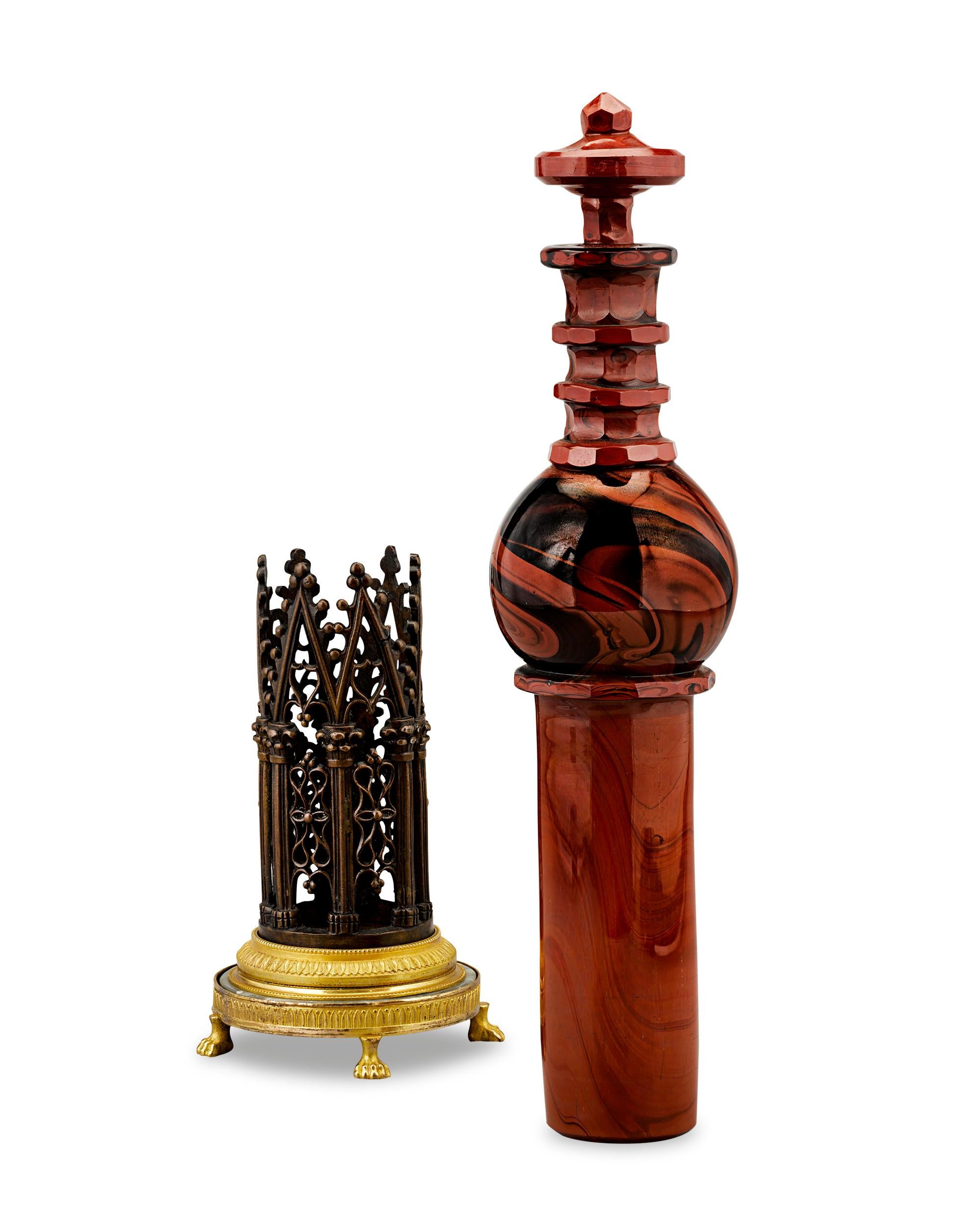 This fascinating Charles X-period “cathedral” flacon has the appearance of agate, but it is actually crafted of rare red hyalite glass. The sculpted vessel rests within a patinated and gilt bronze basilica-inspired stand decorated in an openwork,