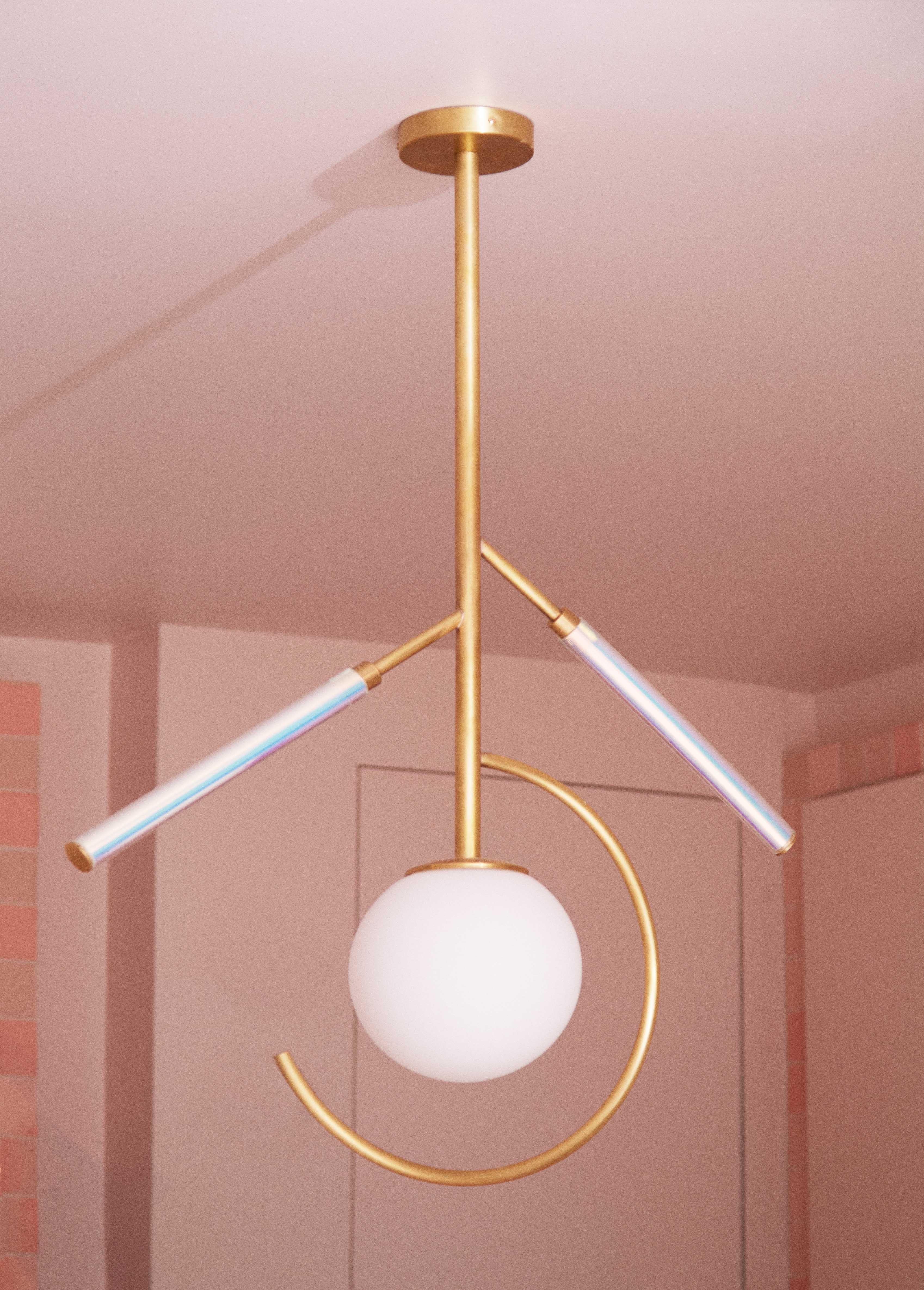Hype Pendant Lamp by Patricia Bustos de la Torre
Dimensions: D 20 x W 75 x H 101 cm.
Materials: White opal glass, transparent methacrylate tubes, iridescent vinyl and brass.

“Hype” lamp is an exciting and vitaminic jewel that combines fluorescents