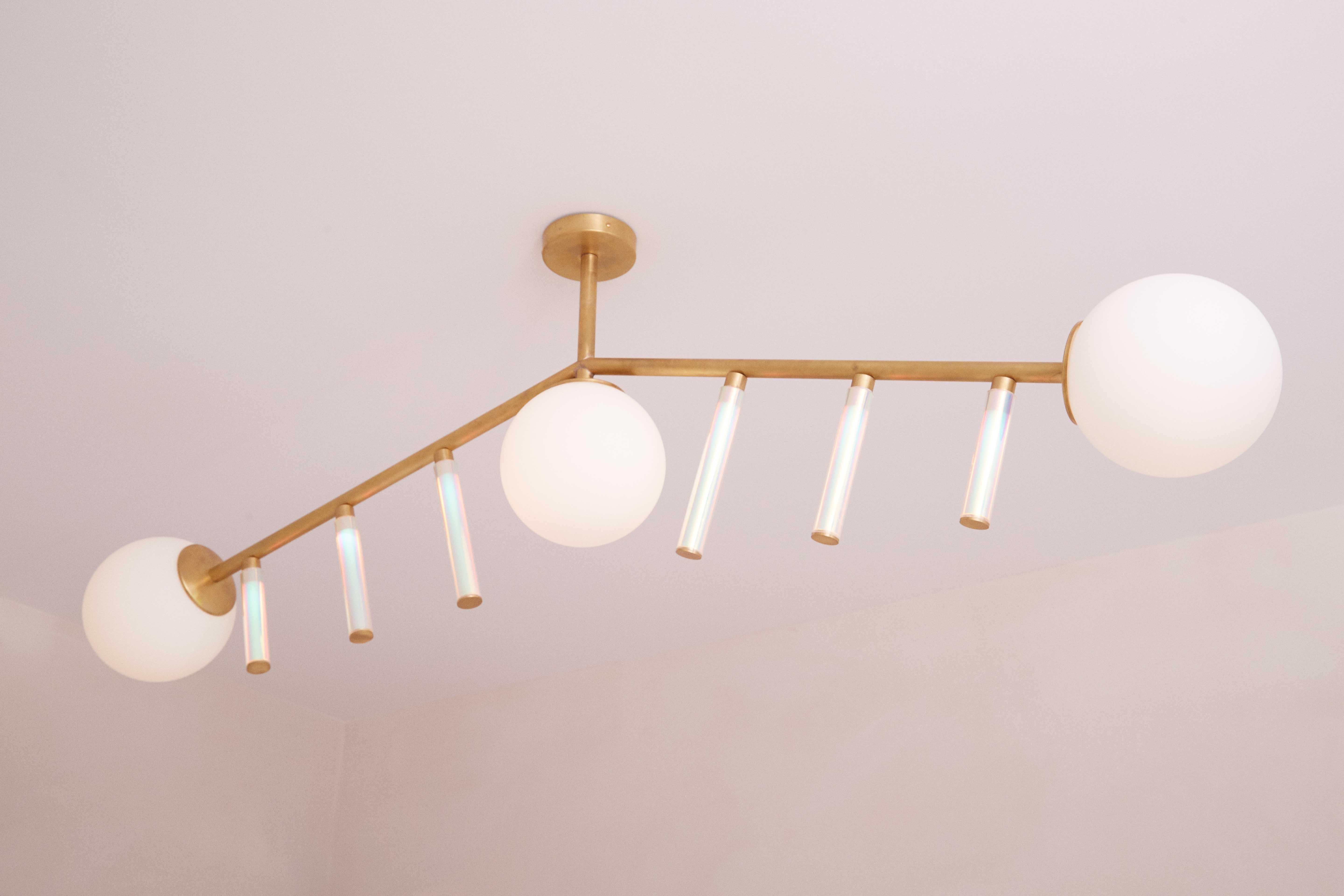 Hype XL Pendant Lamp by Patricia Bustos de la Torre
Dimensions: D 20 x W 161 x H 110 cm.
Materials: White opal glass, transparent methacrylate tubes, iridescent vinyl and brass.

Hype L Chandedier is a two brassed armed hanging jewel, holding three