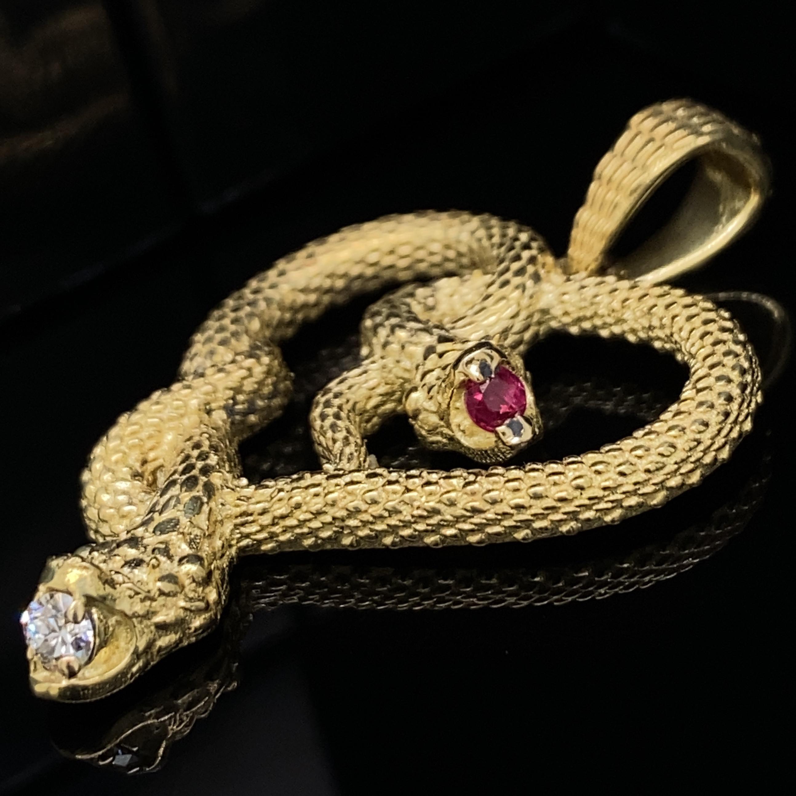 This 18 karat gold pendant is a new design by Eytan Brandes.  It depicts two amorous snakes slithering together to form a heart while they chomp happily on precious gems.  

The smaller snake has a vivid pink ruby (0.75 carats) while the larger
