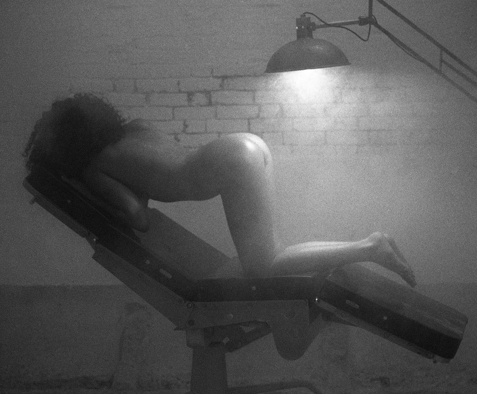 Nadia - Signed limited edition archival pigment print  -  Edition of 5
Sexy photo shoot of a woman in profile, hunched over an old dentist's chair with a subdued, smoky atmosphere, a very grainy photo.
Provenance : Ian Sanderson’s Estate

This image