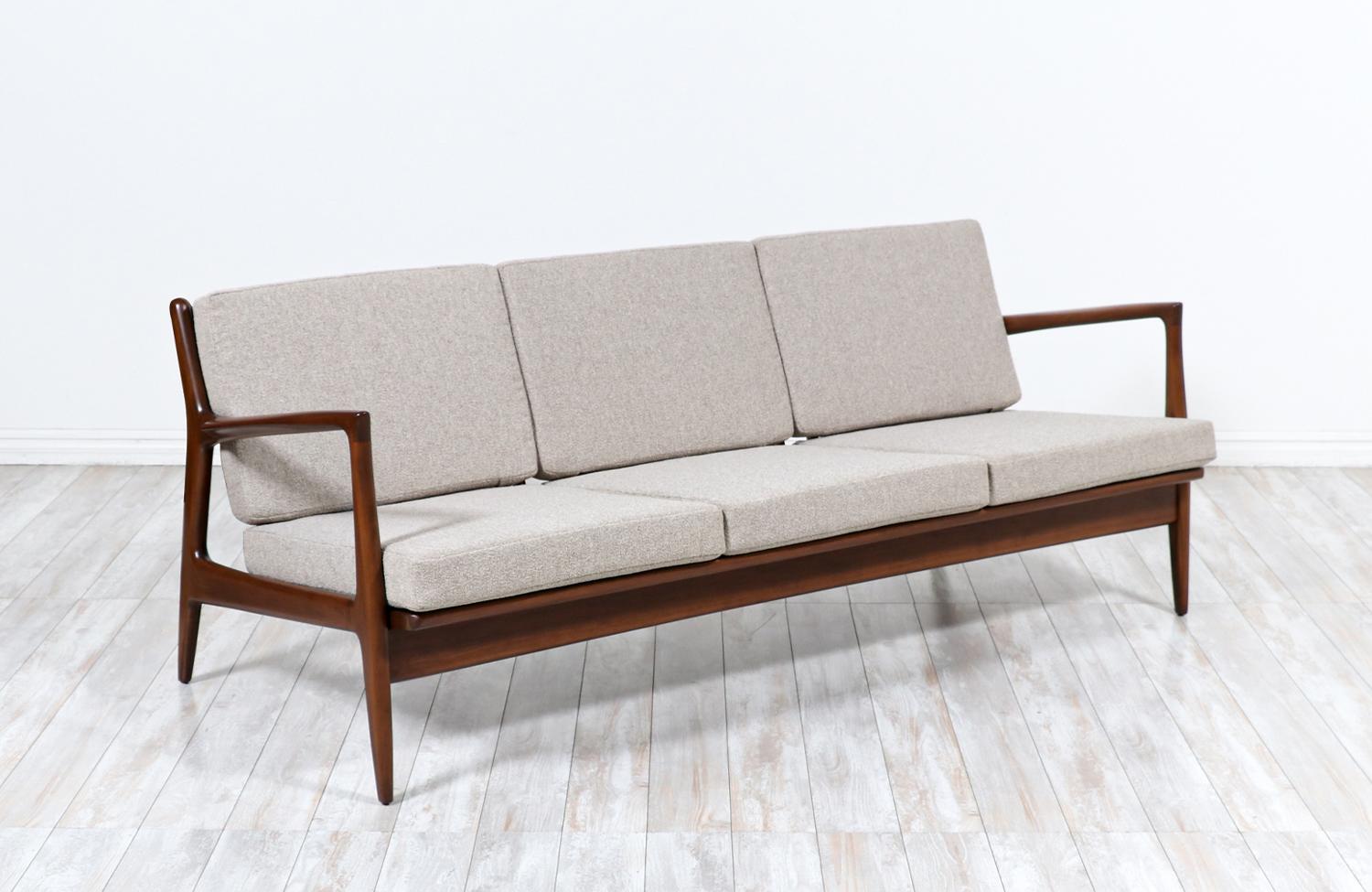Stylish modern sofa designed by Danish architect and furniture designer Ib-Kofod Larsen for Selig in Denmark circa 1960s. This elegant sofa features a solid sculpted walnut-stained Beechwood frame with vertical slats at the back to create a sleek