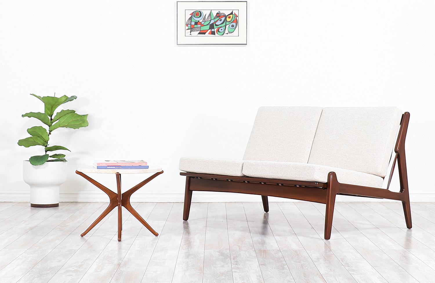 Elegant modern love seat designed by Danish architect and furniture designer Ib-Kofod Larsen for Selig in Denmark, circa 1960s. This beautiful and compact sofa features a solid sculpted walnut-stained Beechwood frame with vertical slats at the back