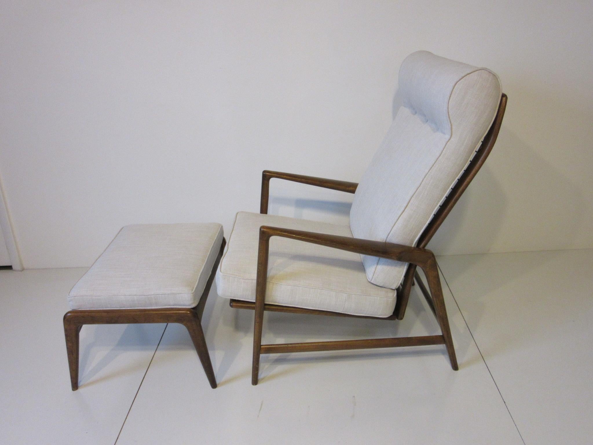 A dark sculptural wood framed lounge chair and matching ottoman upholstered in a darker cream linen fabric. The chair has a four way adjustable reclining backside using a small cast brass knob to one side which gives you more options for comfort,