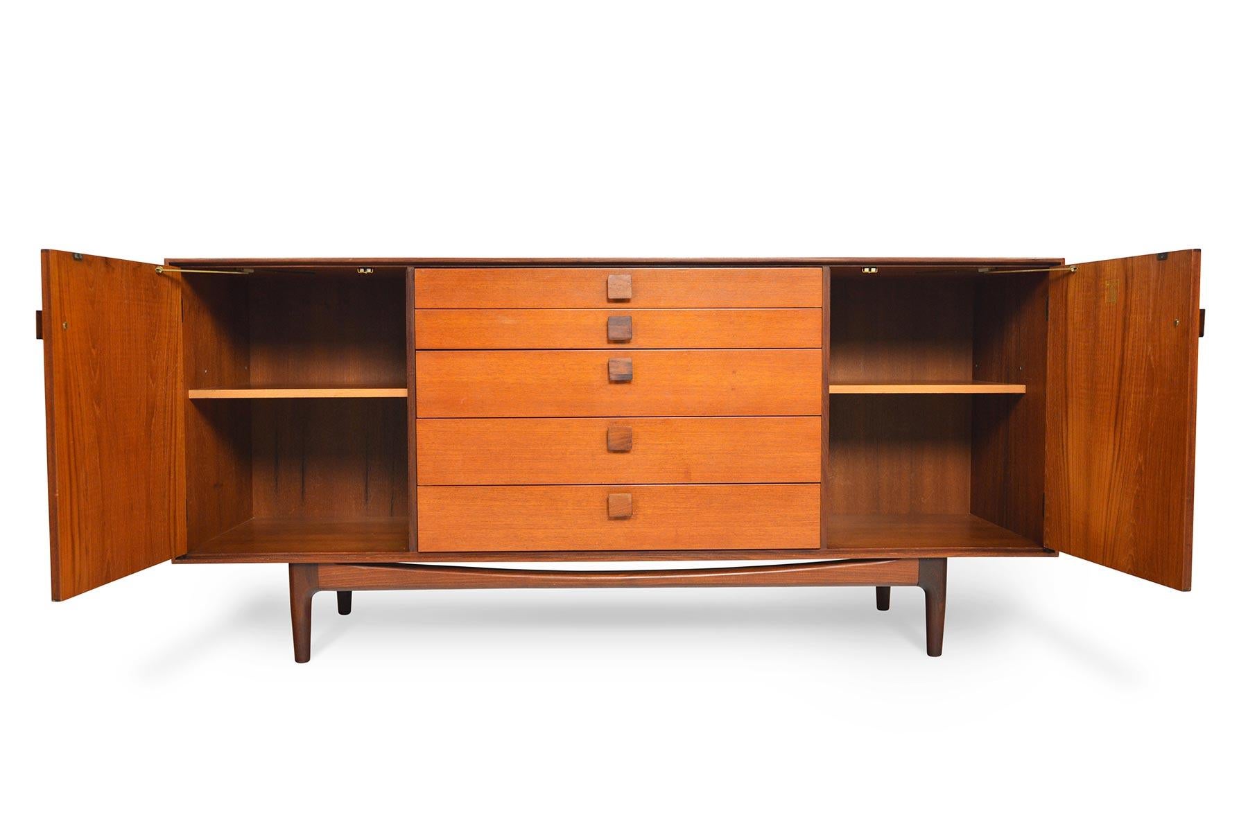 This medium midcentury teak credenza was designed by Ib Kofod Larsen for G Plan in 1961 for the Danish Range. Crafted in teak and afrormosia with handsomely refined lines, two wide doors open to reveal two bays with adjustable shelving. A bank of