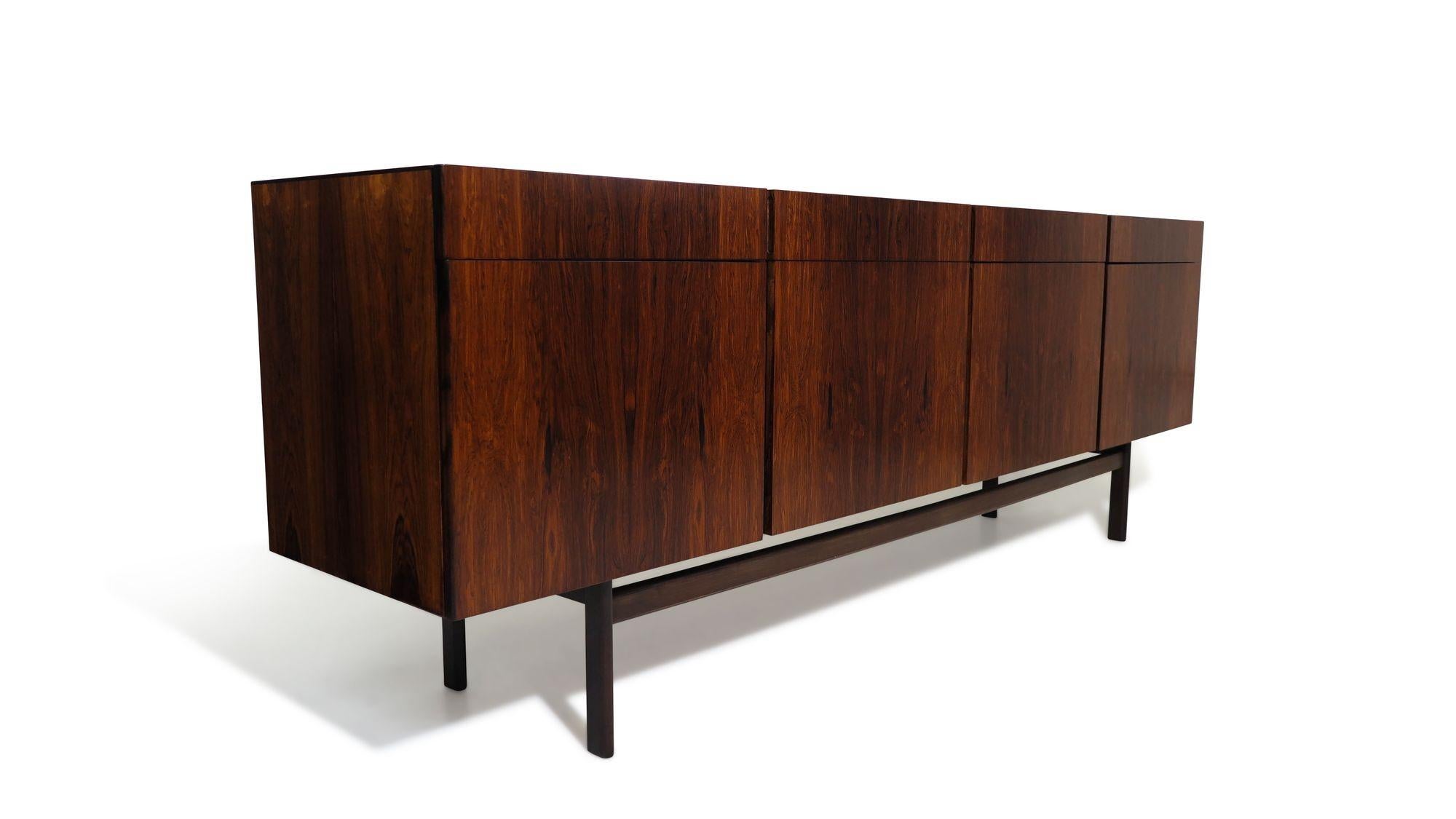 Mid-century Rosewood credenza designed by Ib Kofod-Larsen, Denmark, 1955. This sideboard features book-matched rosewood with four cabinet doors below four drawers. Upon opening, the doors reveal an oak interior with adjustable shelves and a series