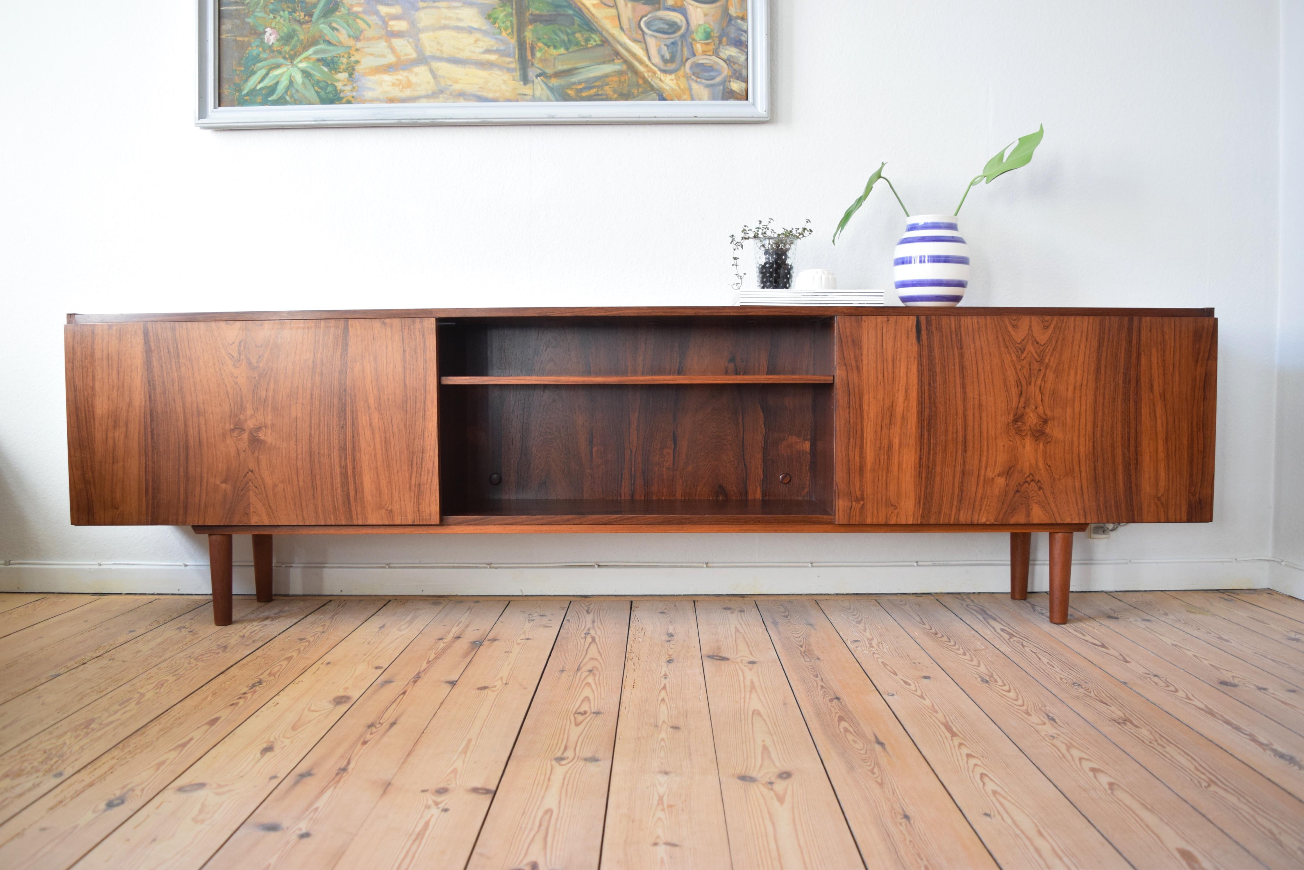 Very long and low rosewood sideboard by Ib Kofod-Larsen manufactured in Denmark in the late 1960s-early 1970s. Two storage spaces with flip-down doors on each side, one with a striking red vinyl interior which can be used as a bar cabinet. The other