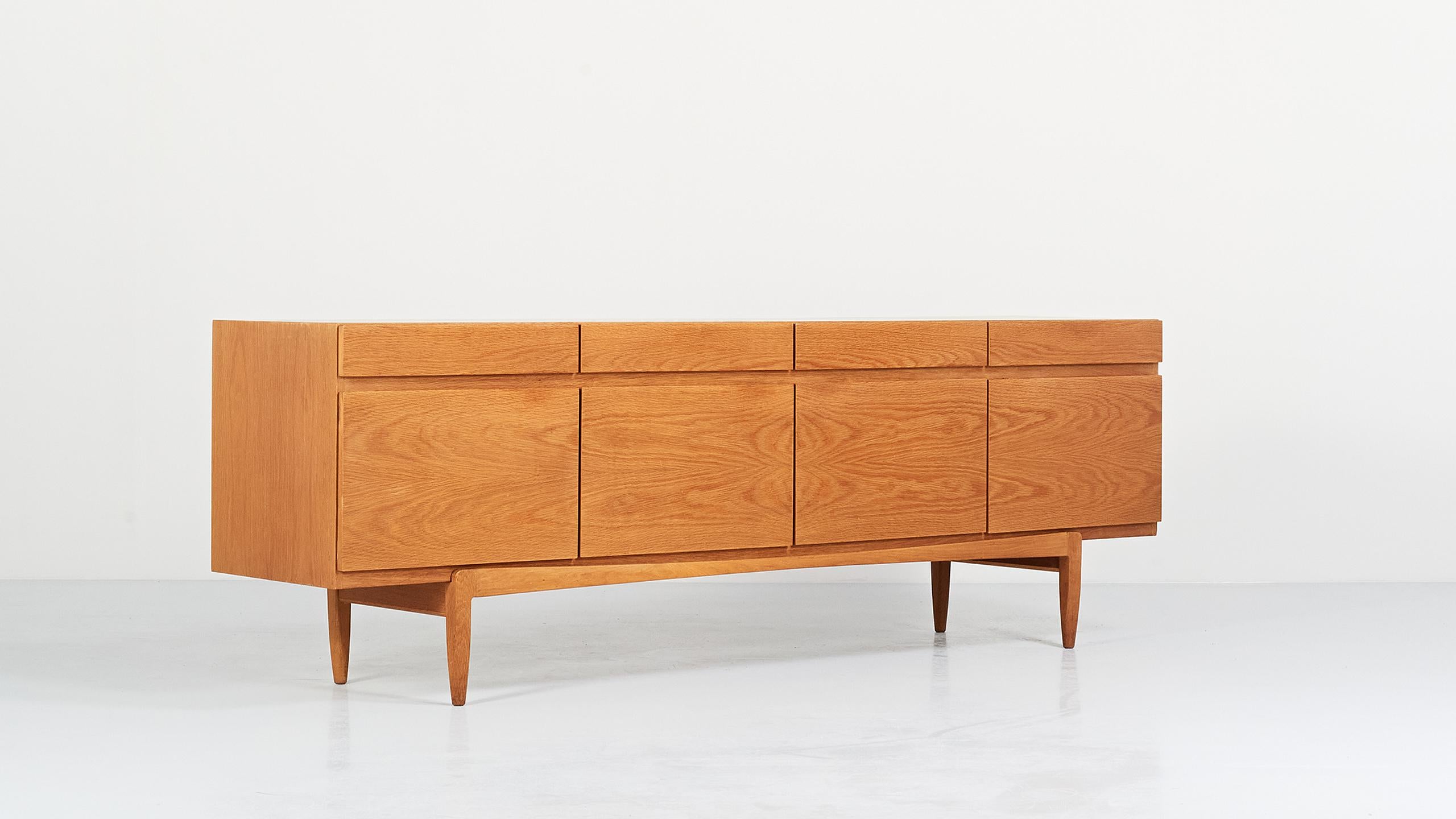 Minimalist sideboard in oak and blond oak veneer, by Danish designer Ib Kofod-Larsen for Faarup Møbelfabrik. Opening with four drawers and four doors revealing drawers and shelves. 

Slight traces of use, very good general condition, Denmark,