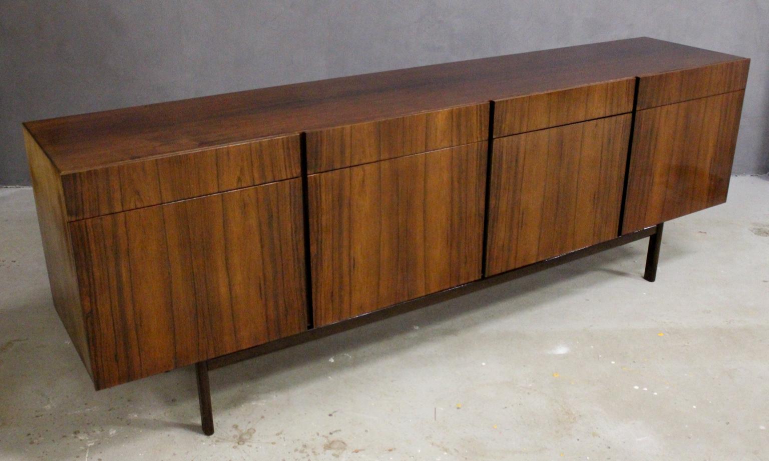 This Ib Kofod-Larsen FA66 can be considered royalty among Danish midcentury design credenzas. This long sideboard is segmented in four drawers and four doors with vibrant rosewood veneer that tickles your senses. The left door hides each three small