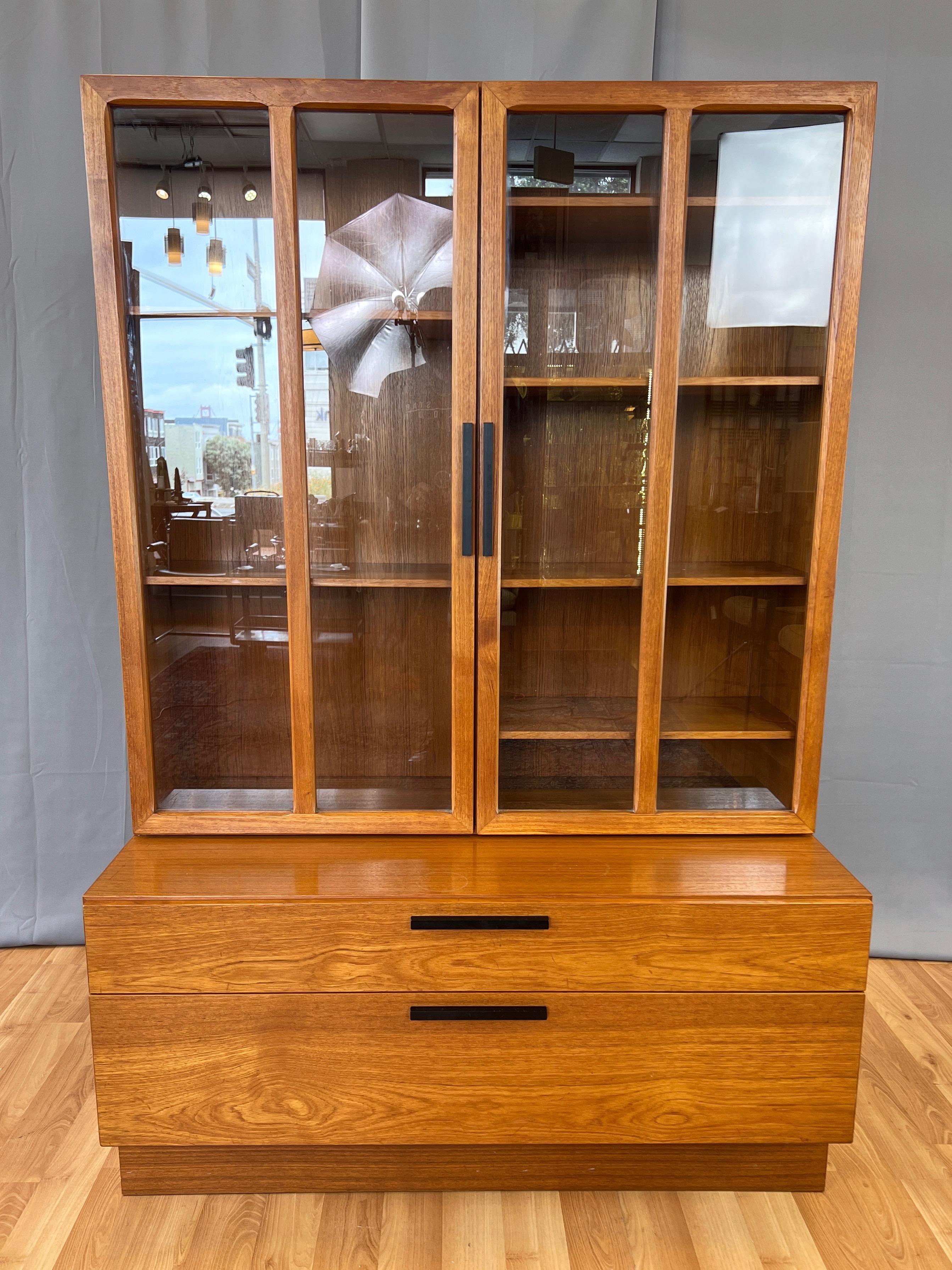 A very handsome and spacious circa 1970 Danish modern teak wall unit by Ib Kofod-Larsen for Faarup Møbelfabrik, comprised of an upper display cabinet with glass doors and adjustable shelves sitting atop a lower cabinet with drawers.

Features the