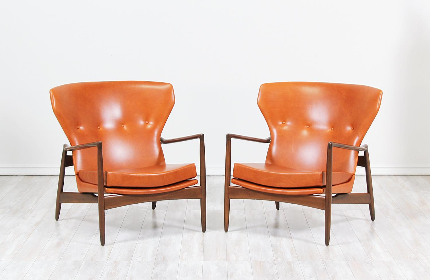 Pair of stylish lounge chairs designed by Ib Kofod-Larsen for Selig in Denmark, circa 1960s. These bold wingback style chairs feature a sculptural walnut-stained beechwood frame that holds the seat with a high-back and lower armrests emphasizing its