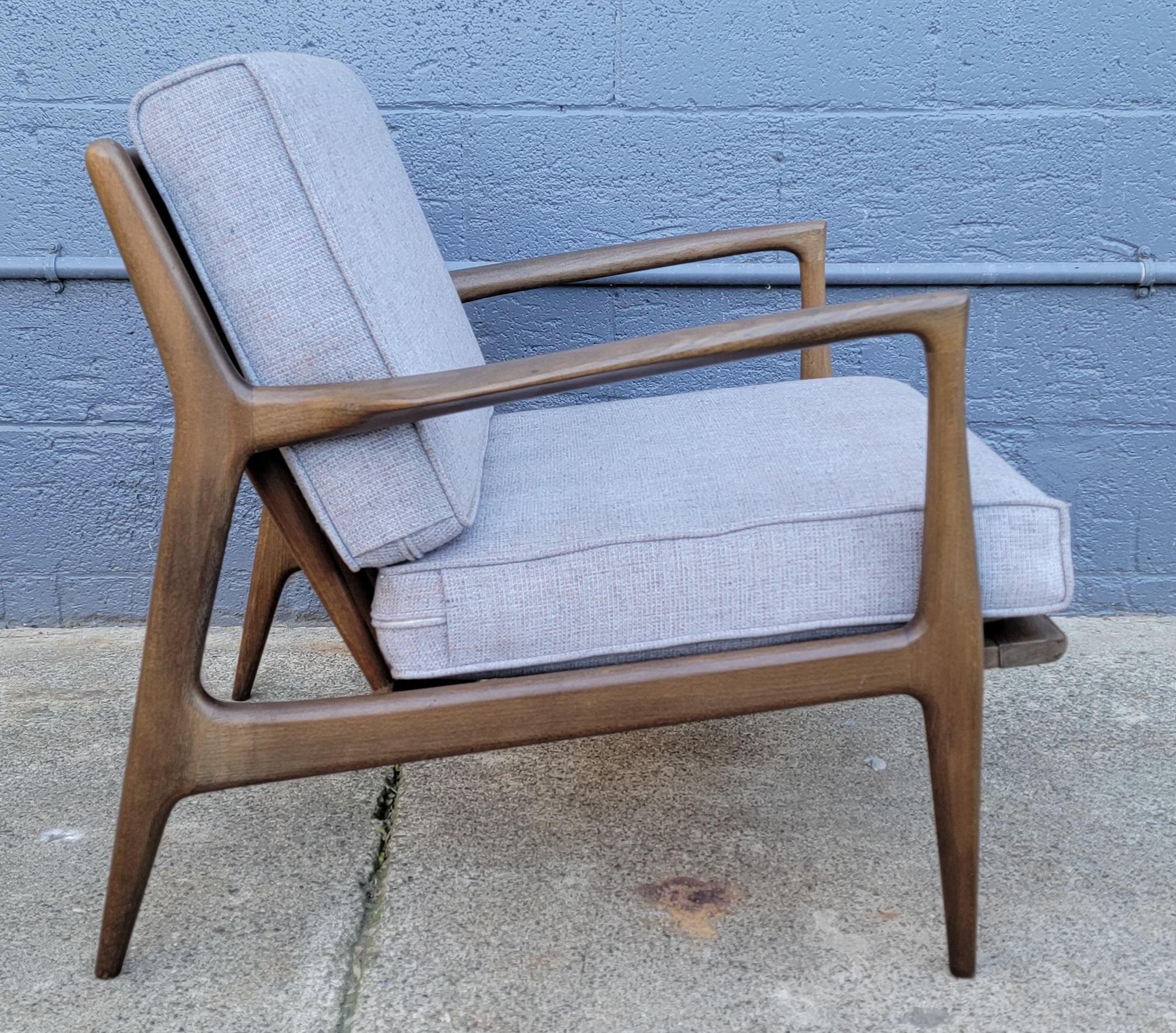 Iconic Danish Modern lounge chair designed by Ib Kofod-Larsen, Denmark 1960's. Original finish with fade and discoloration, older re-upholstery to reversible cushions in good condition. Fagas straps show signs of wear and some sagging. Structurally