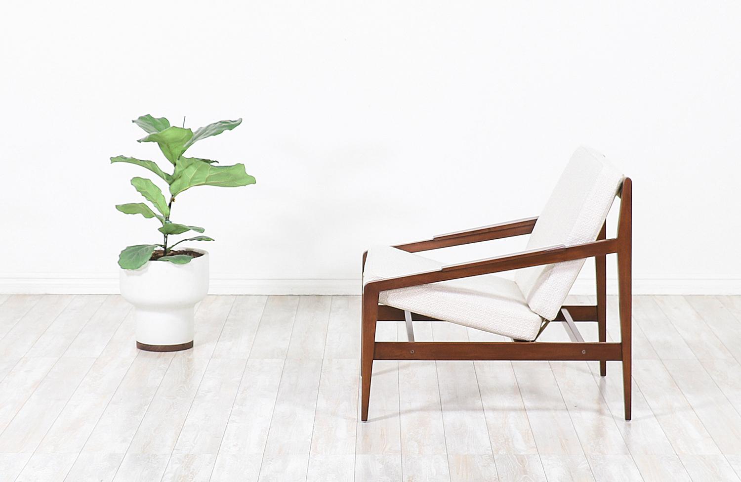 Elegant modern lounge chair designed by Ib Kofod-Larsen for Selig in Denmark, circa 1960s. This beautiful ergonomic lounge chair features a sturdy walnut-stained beech-wood frame with an angled seat and back that is held in place by new Pirelli
