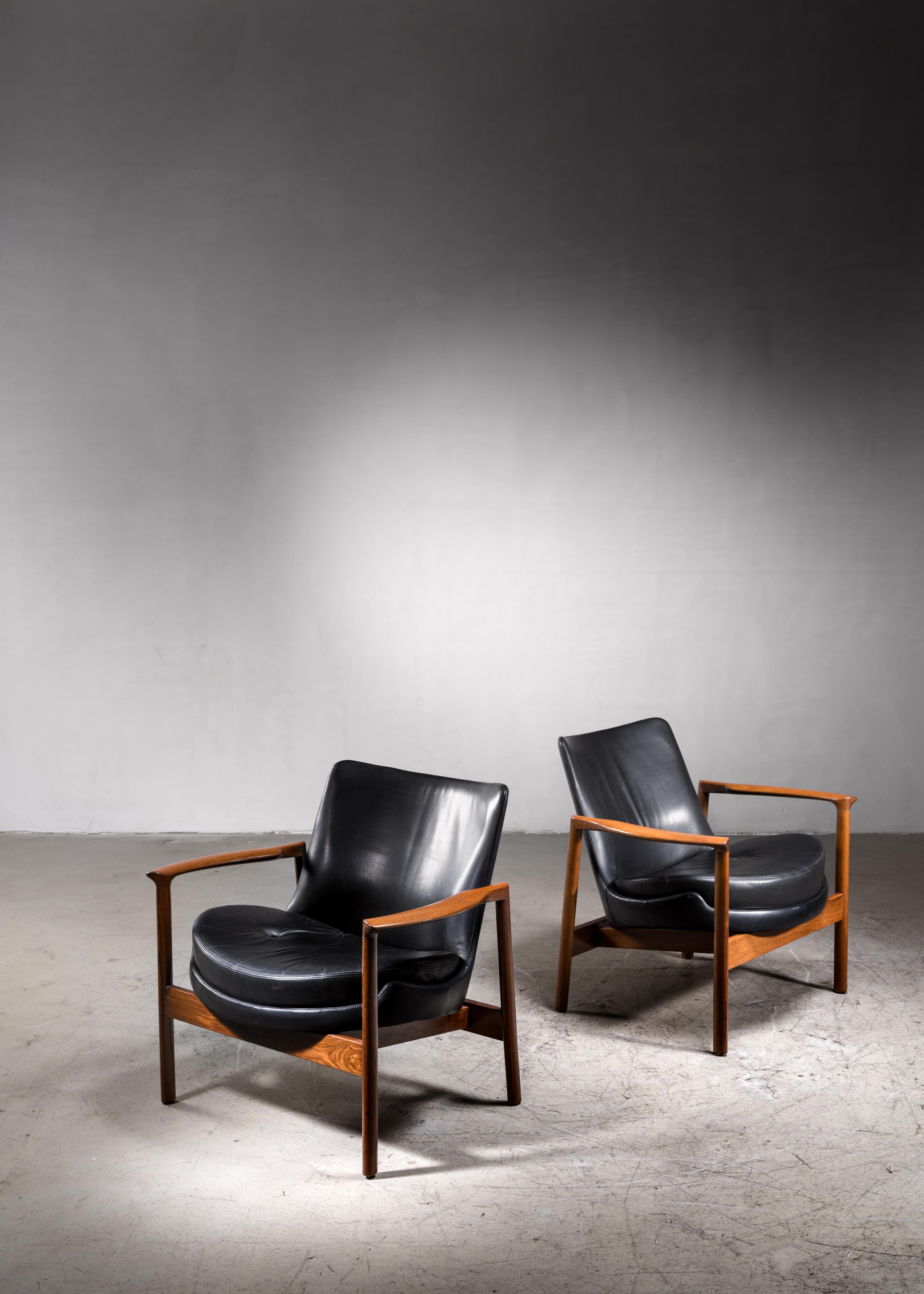Ib Kofod-Larsen Lounge Chairs, an adaption of the Elizabeth chair commissioned for Forscher. The chairs are made of a walnut frame with curved armrests and a black leather upholstery with a loose cushion.
This is an adapted version of the Elizabeth