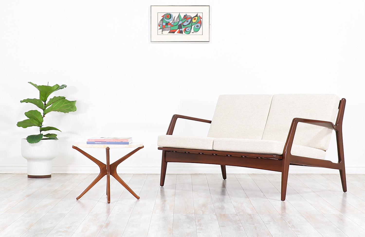 Stylish two-seat modern love seat designed by Danish architect and furniture designer Ib-Kofod Larsen for Selig in Denmark, circa 1960s. This elegant and compact sofa features a solid sculpted walnut-stained beechwood frame with armrests on both