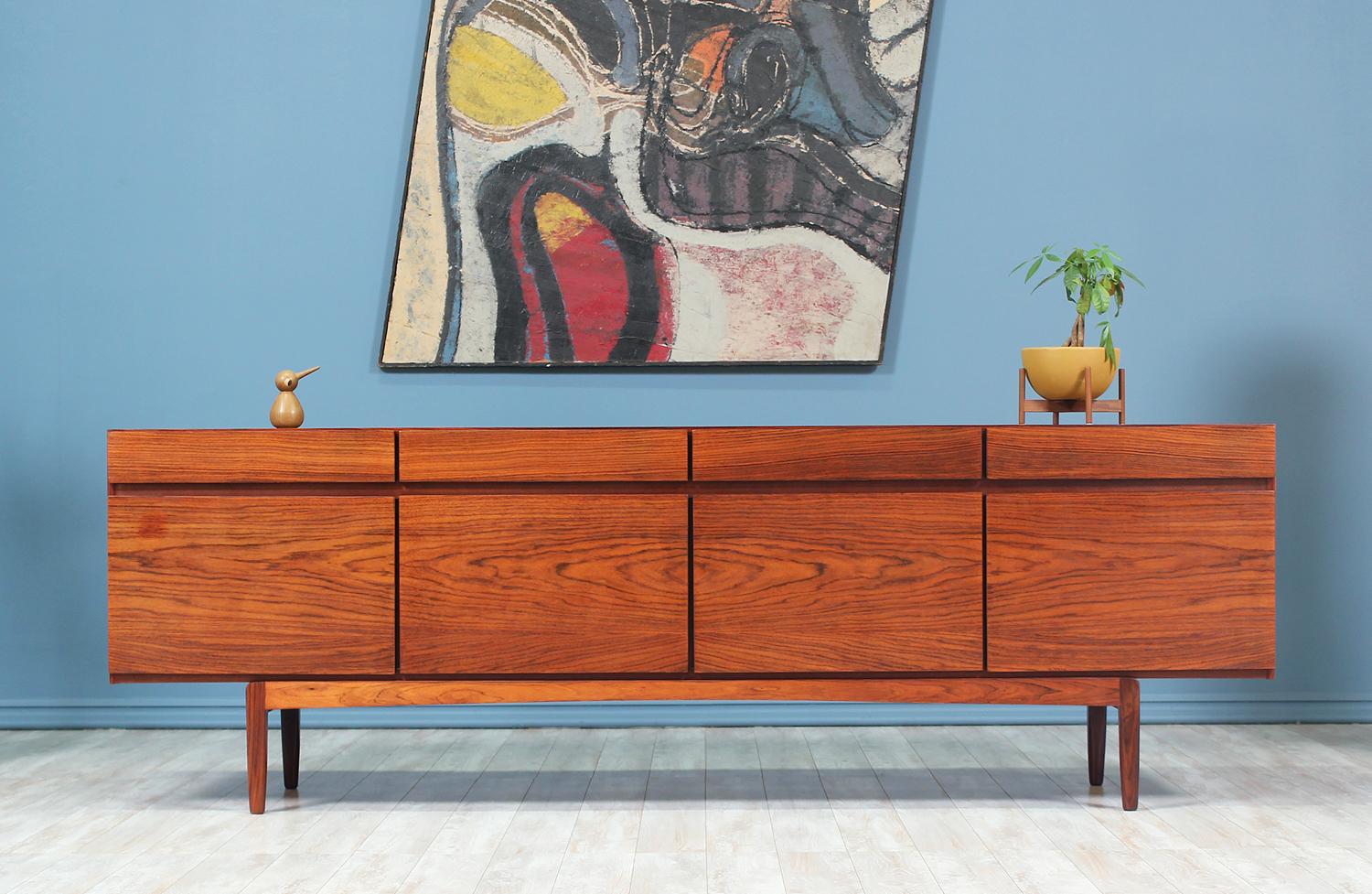 Elegant credenza designed by Ib Kofod-Larsen for Faarup Møbelfabrik in Denmark, circa 1950s. This credenza is comprised of a sturdy rosewood case with a gorgeous and intricate grain on the front and throughout. It features four push-open doors that