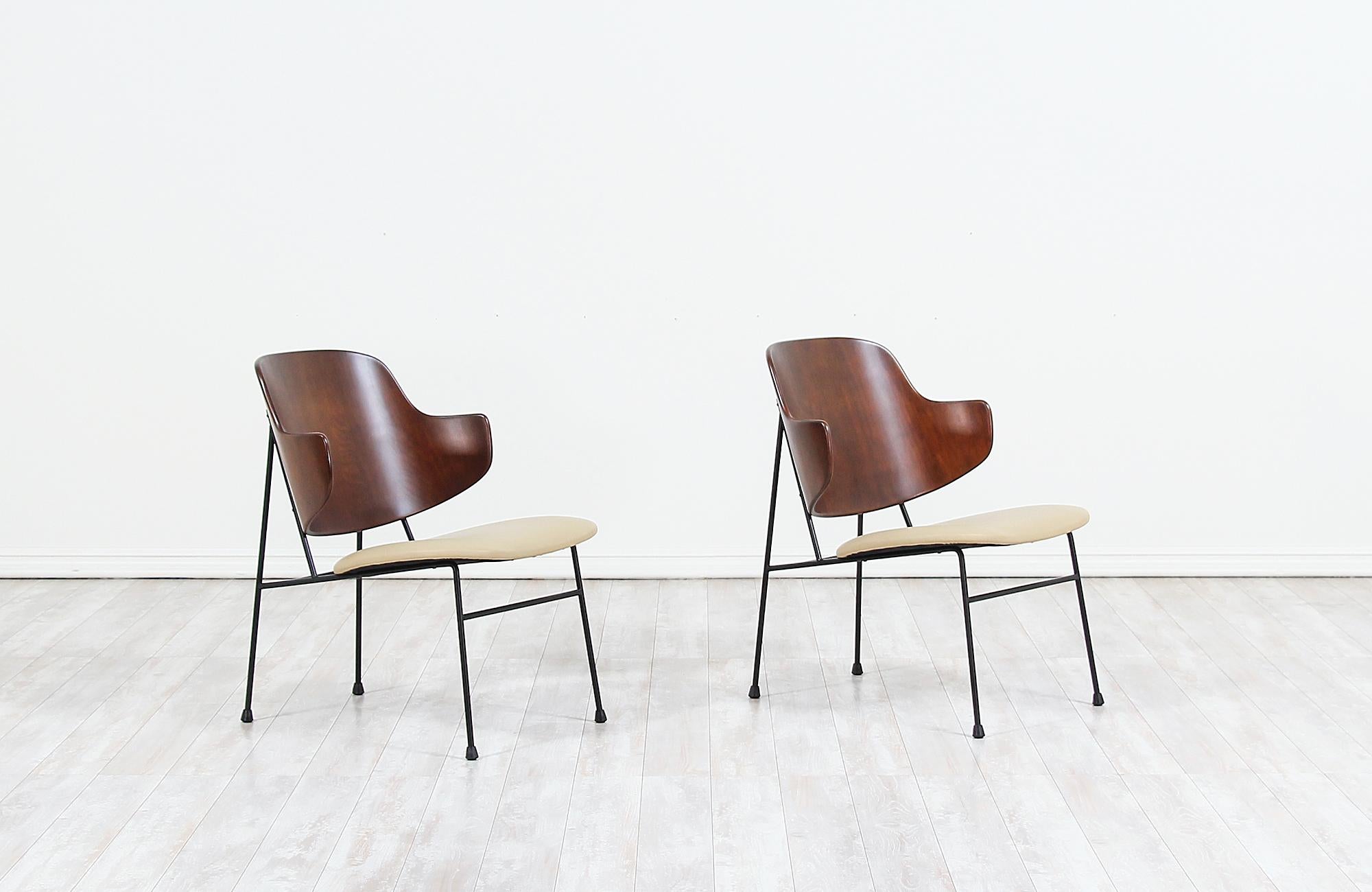 Iconic pair of ‘Penguin’ modern lounge chairs designed by Ib Kofod-Larsen for Selig in Denmark, circa 1960s. These timeless Danish modern chairs feature a structurally sound black iron frame that supports the newly refinished molded bentwood