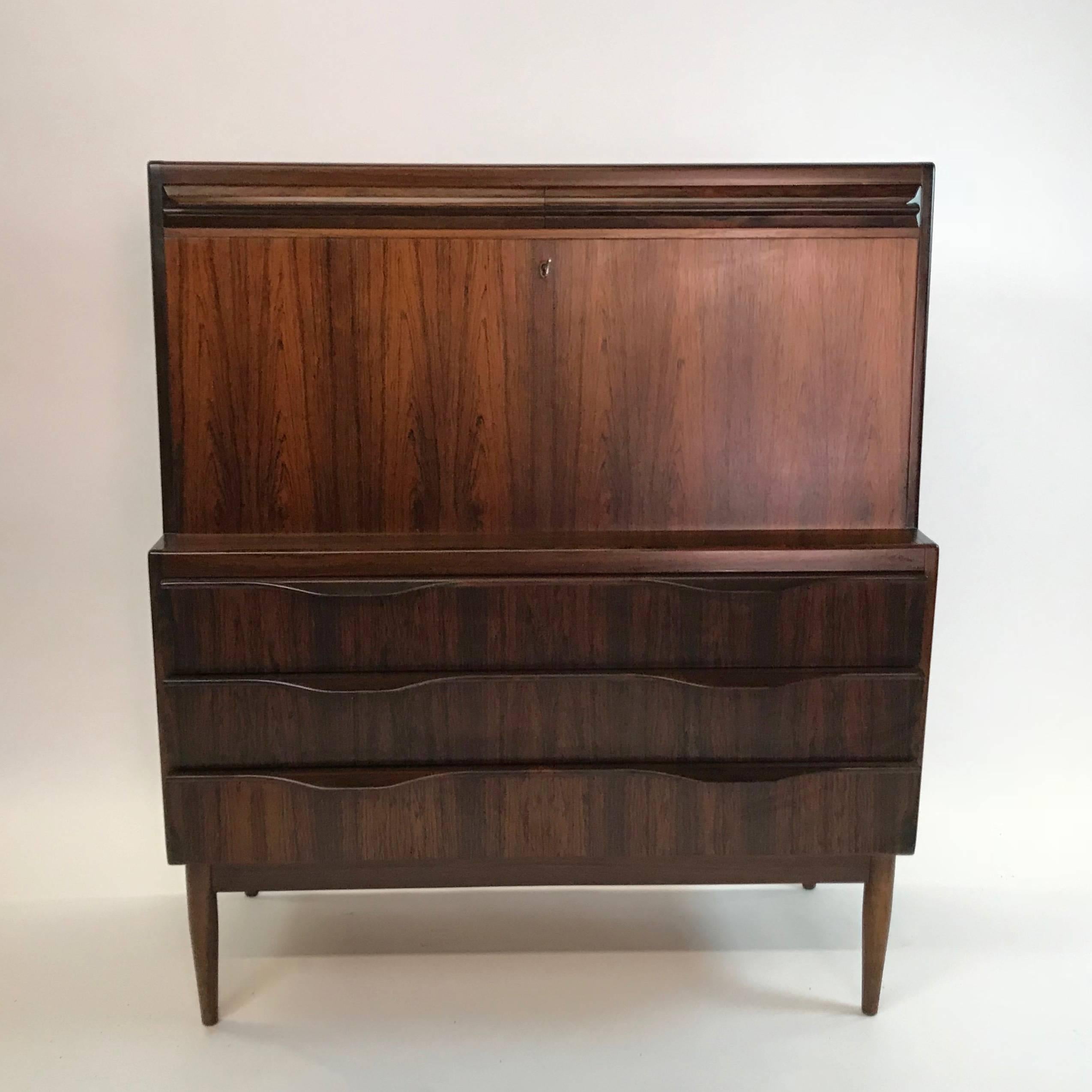Scandinavian Modern, secretary cabinet by Ib Kofod-Larsen features a rare, exotically grained rosewood finish with beautifully sculpted drawer handles and tapered legs. The top front opens into a desk space revealing a variety of drawers, shelves