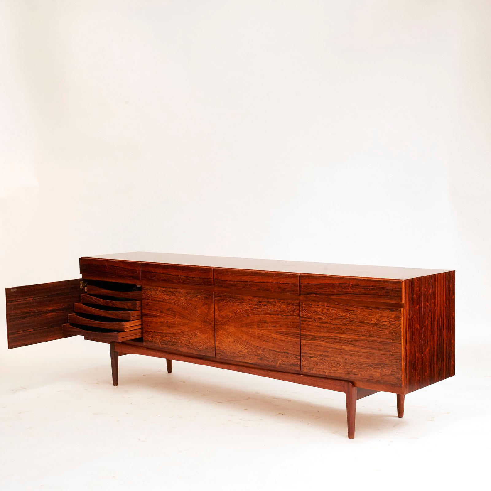 A Danish rosewood sideboard designed by Ib Koford-Larsen (1921-2003) and produced Faarup Møbelfabrik, with striking well matched veneers, four cupboard doors over four drawers. Drawers inside fitted with green felt. 

