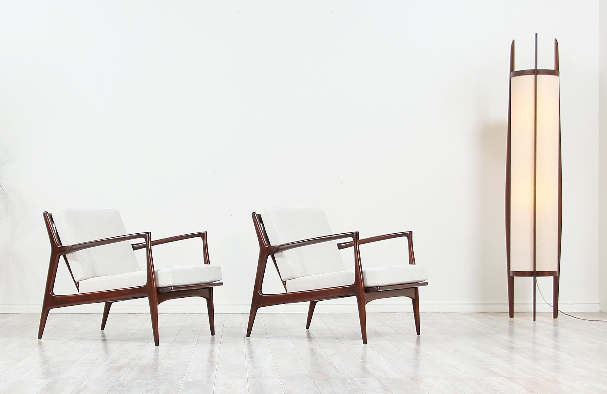 Pair of sleek lounge chairs designed by Ib Kofod-Larsen for Selig in Denmark, circa 1960s. These elegant ergonomic lounge chairs feature a sturdy walnut-stained beechwood frame with angled legs and a sculptural slatted back that is held in place by