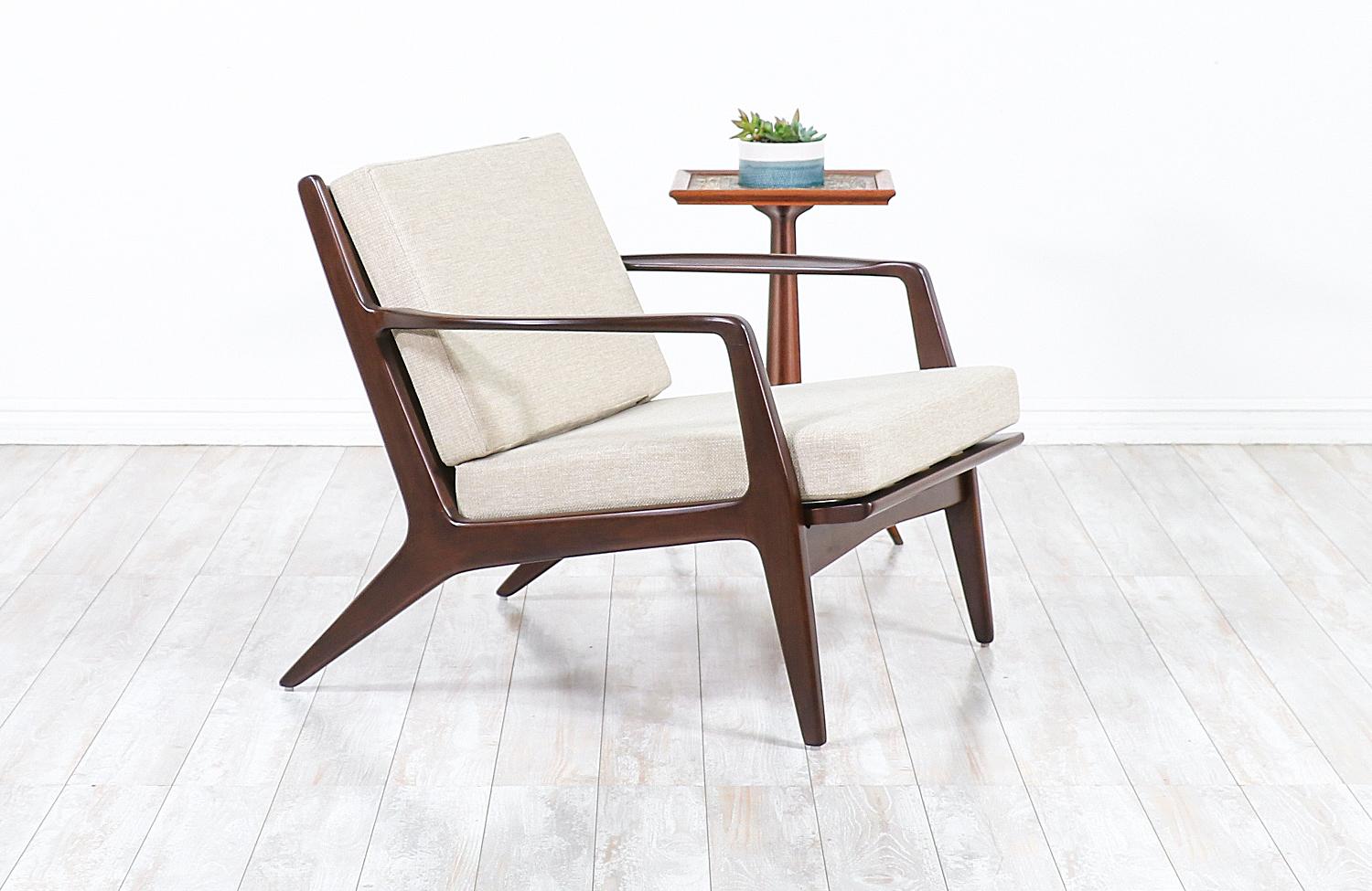 Stylish lounge chair designed by Ib Kofod-Larsen for Selig in Denmark, circa 1960s. This sleek and ergonomic lounge chair features a sturdy walnut-stained beechwood frame with angled legs and a sculptural slatted back that is held in place by bowed