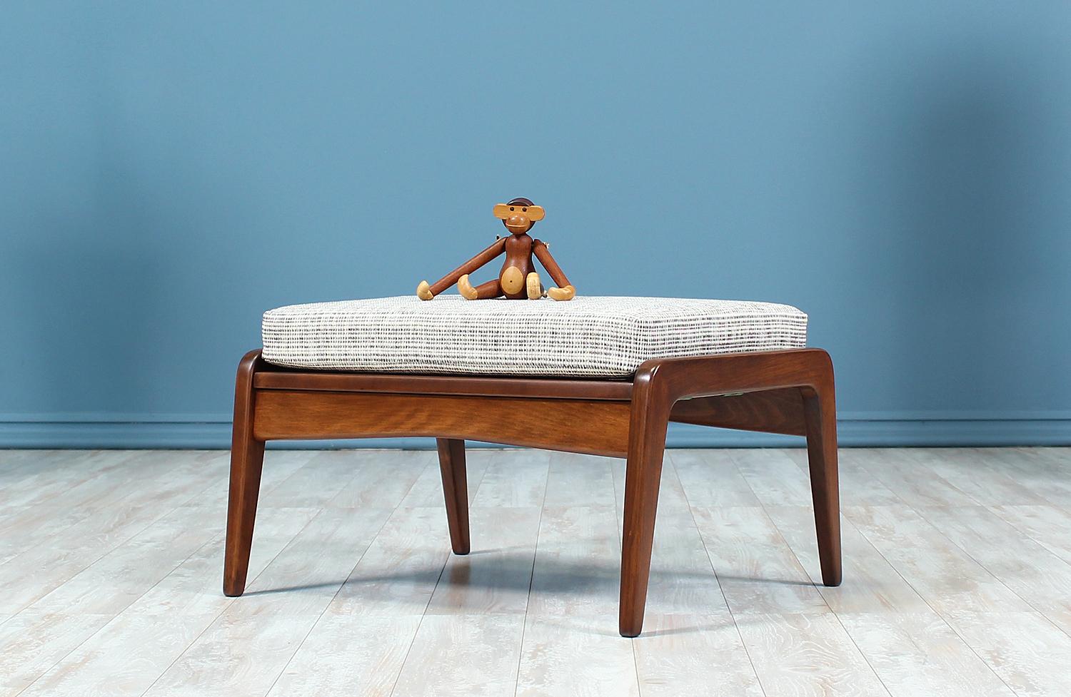 A beautiful stool or ottoman designed by Ib Kofod-Larsen for Selig in Denmark circa 1960’s. This compact and versatile piece features a solid walnut-stained beech wood frame and a comfortable new foam cushion upholstered with a textured grey tweed