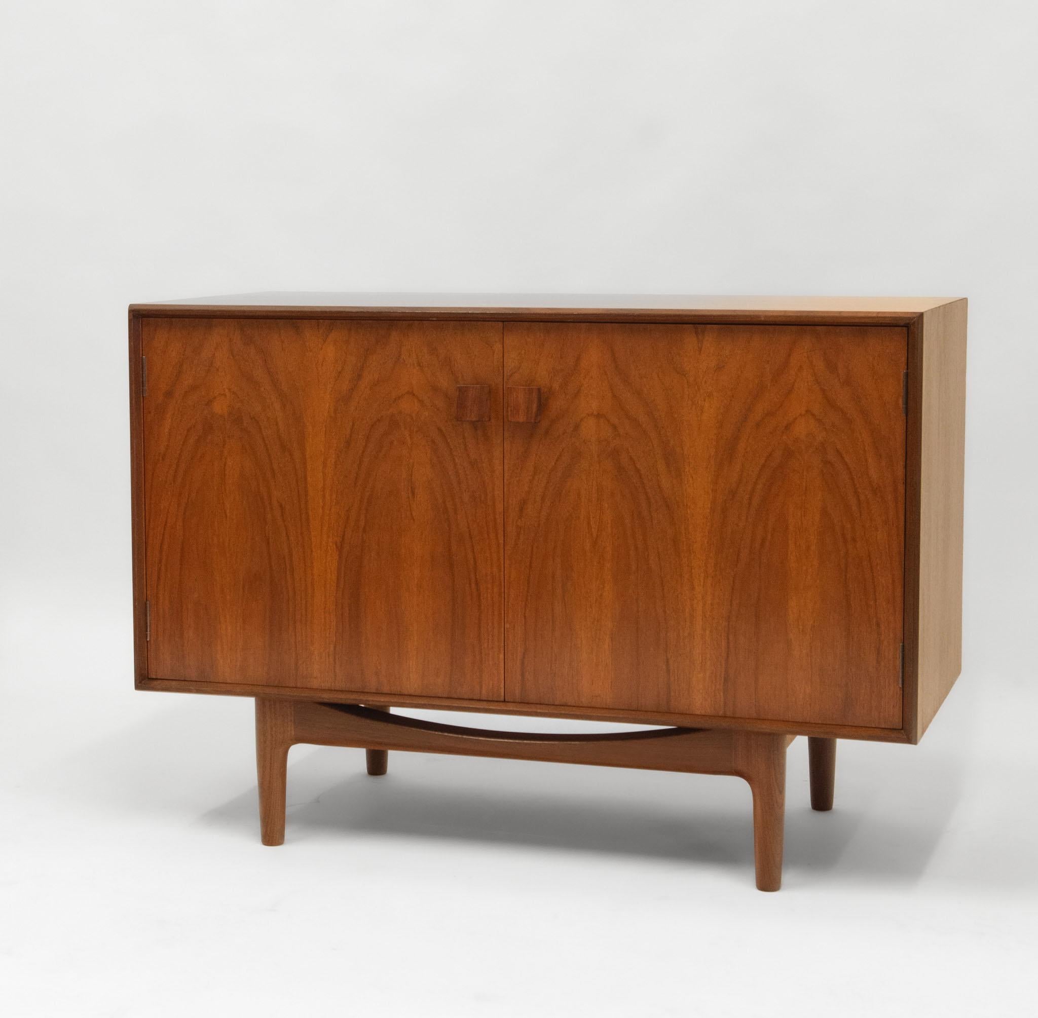 Mid Century teak cabinet by Danish designer Ib Kofod-Larsen (1921-2003) for G-Plan. Circa early 1960's.

The cabinet's two doors have a highly figured book match design, with solid rosewood square form handles. The cabinet sits on a stylized open