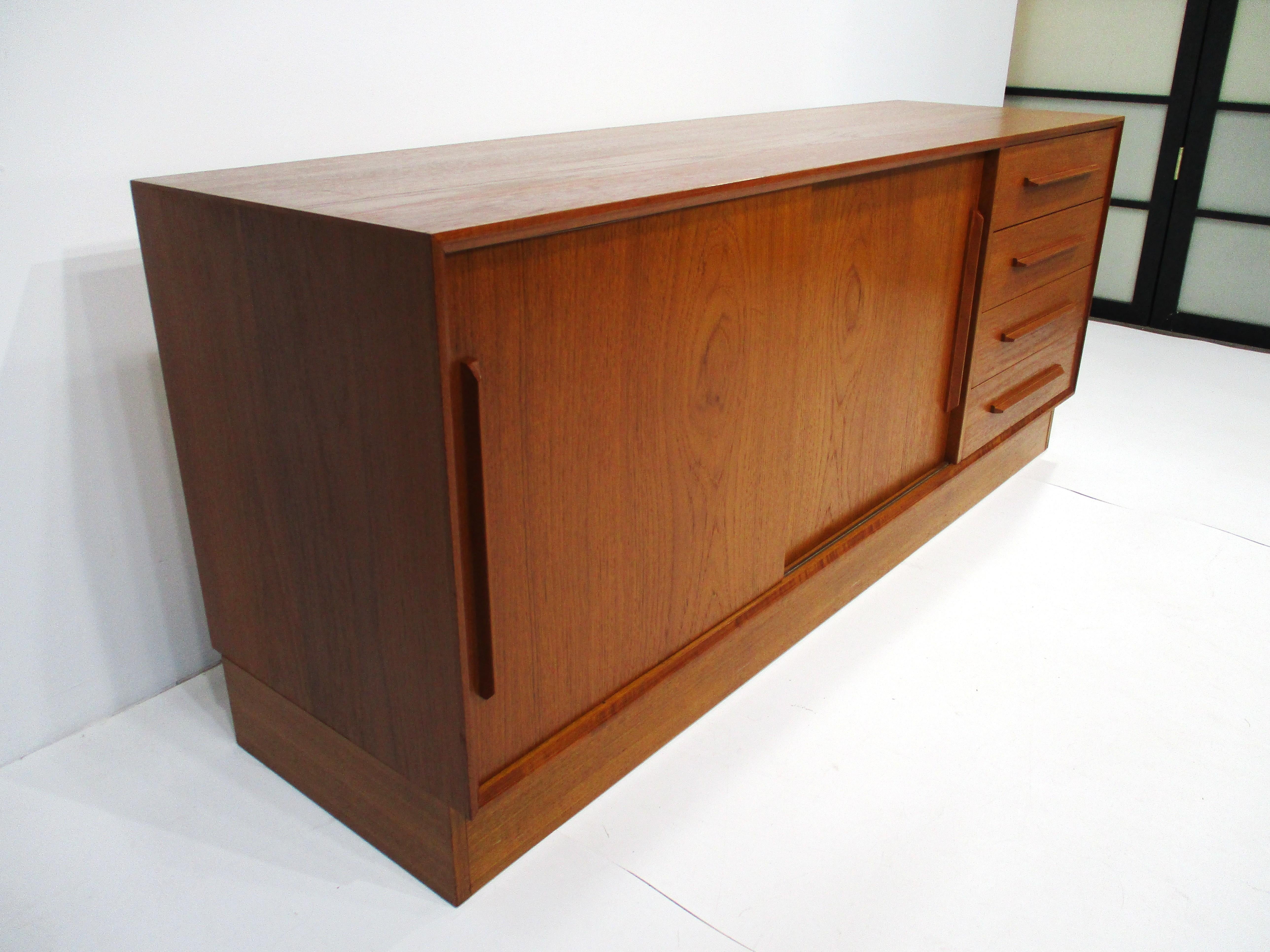 A teak wood credenza or sideboard with double sliding doors and adjustable shelves. The other side has four drawers having nice long pulls for easy access making for a very functional and attractive piece for any room setting. Designed by Ib Kofod